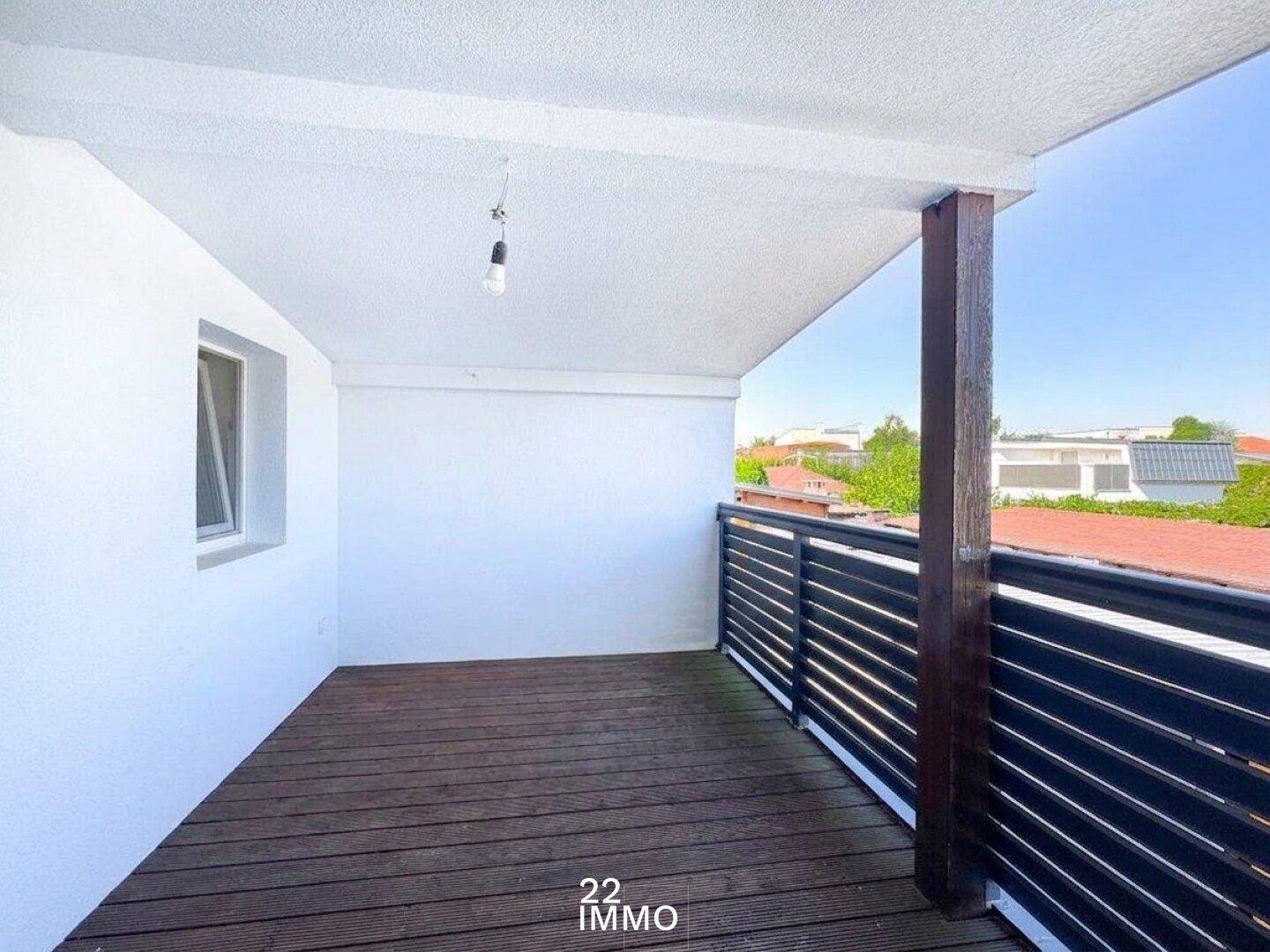 Großer, überdachter Balkon mit Holzboden und dunklem Geländer, ideal zum Entspannen im Freien.