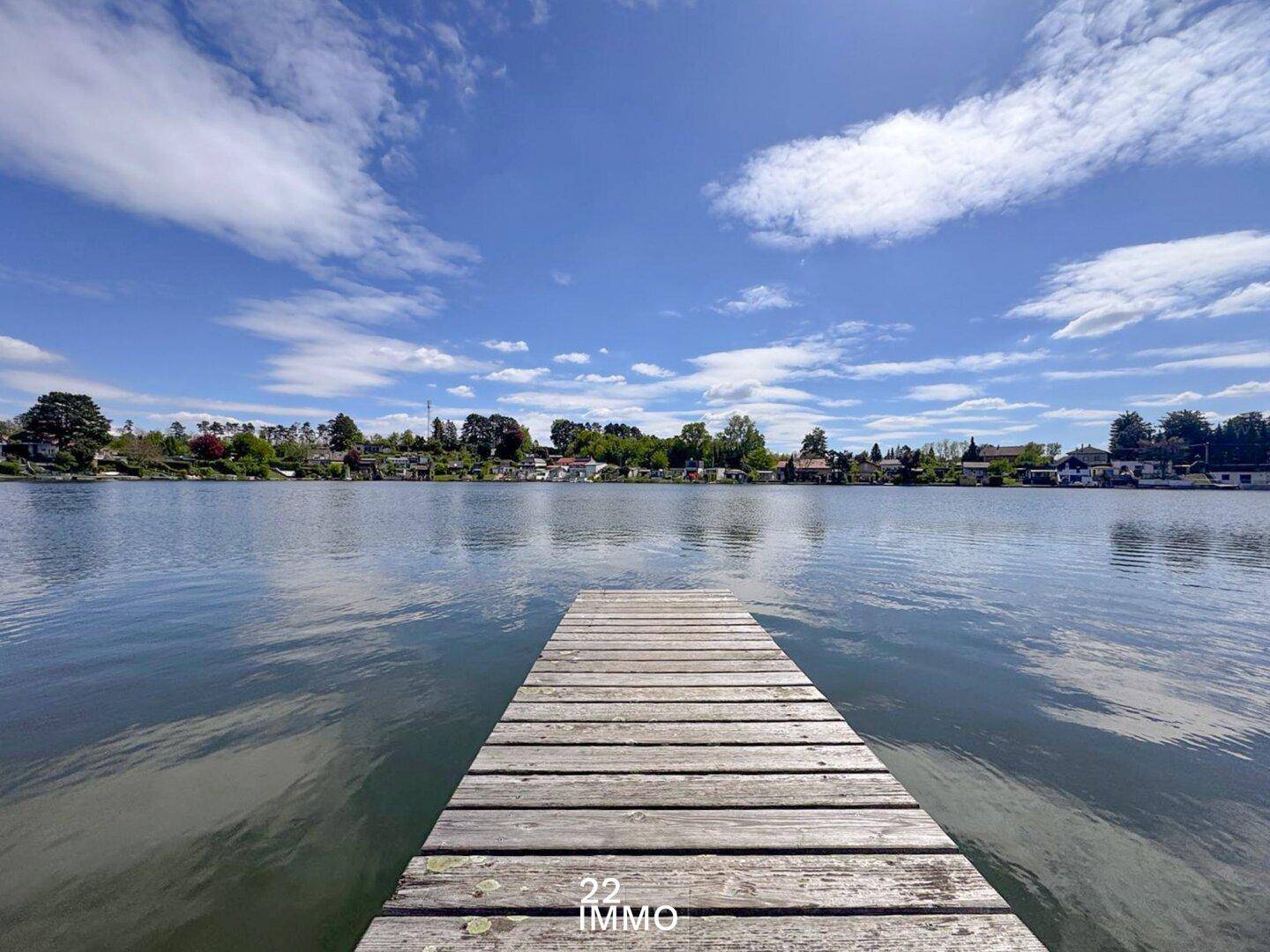Holzsteg führt in den ruhigen See mit weitem Blick auf die gegenüberliegende Uferseite.
