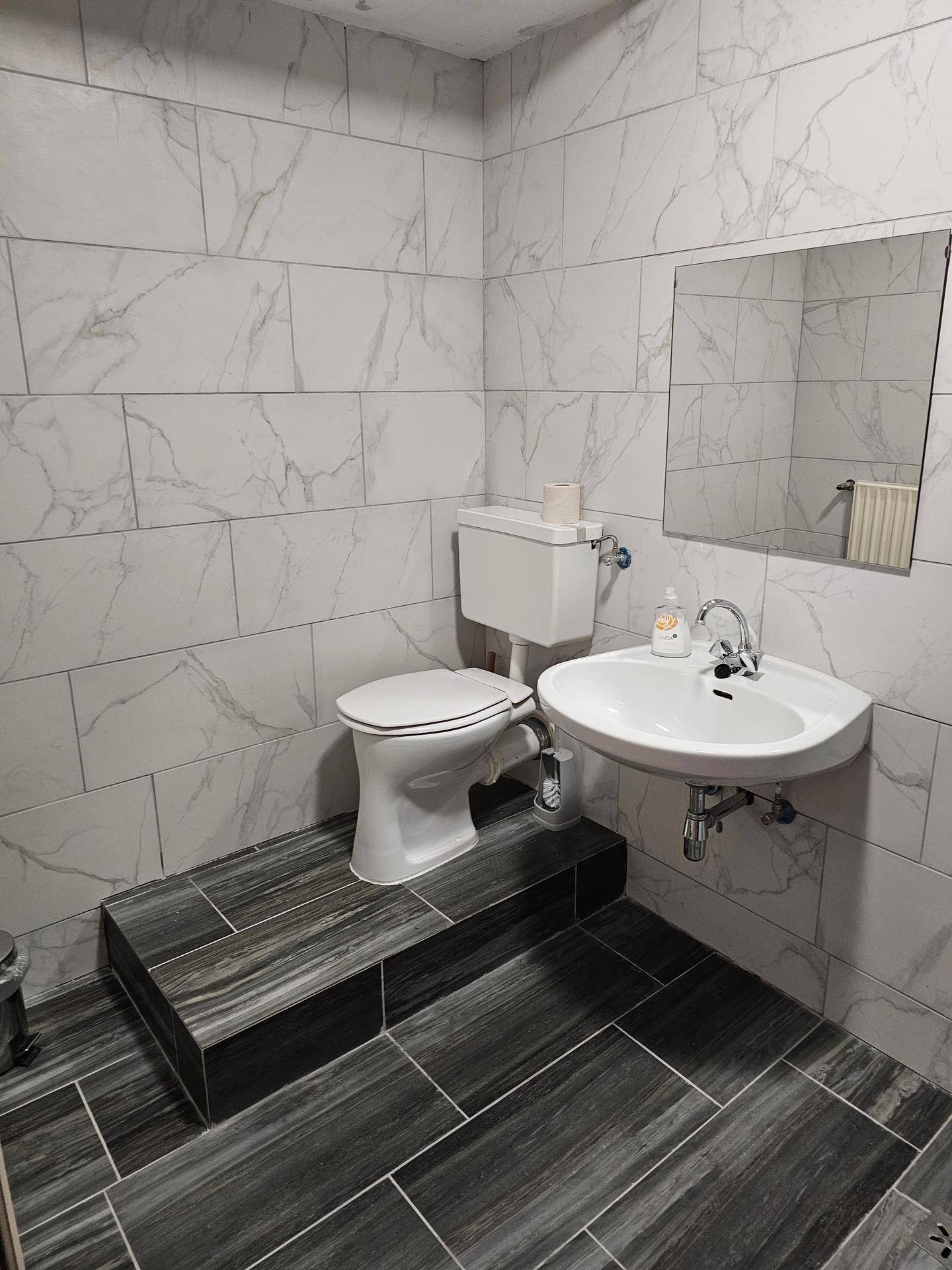 Modernes Badezimmer mit weißen Marmorfliesen an den Wänden und dunklen Holzoptikfliesen auf dem Boden.