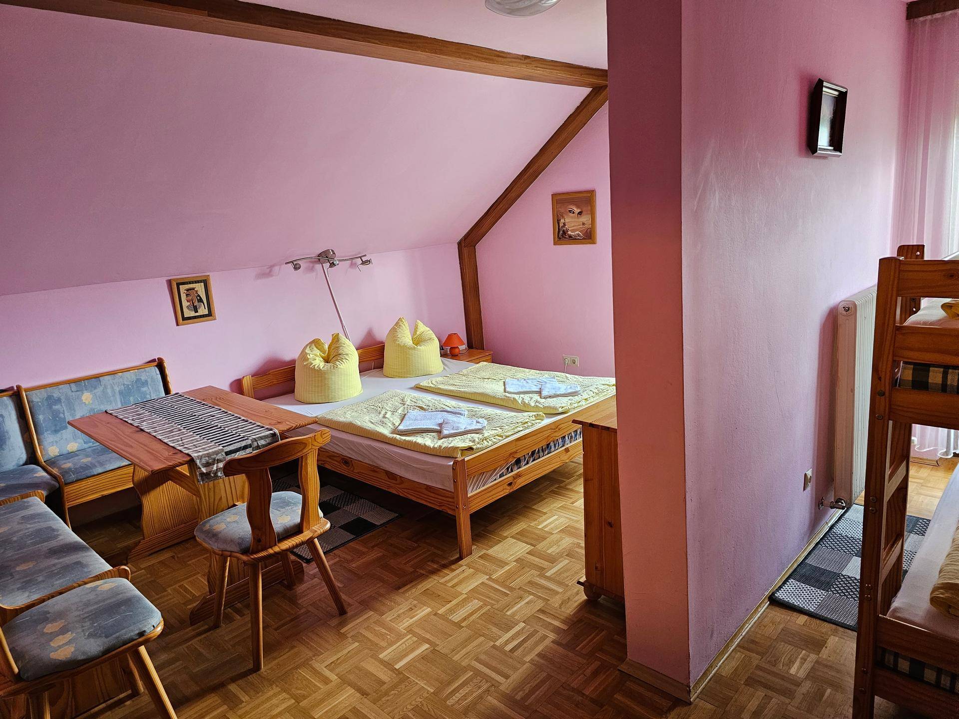 Geräumiges Schlafzimmer mit Doppelbett, Etagenbett, Essbereich und rosa Wänden unter der Dachschräge.