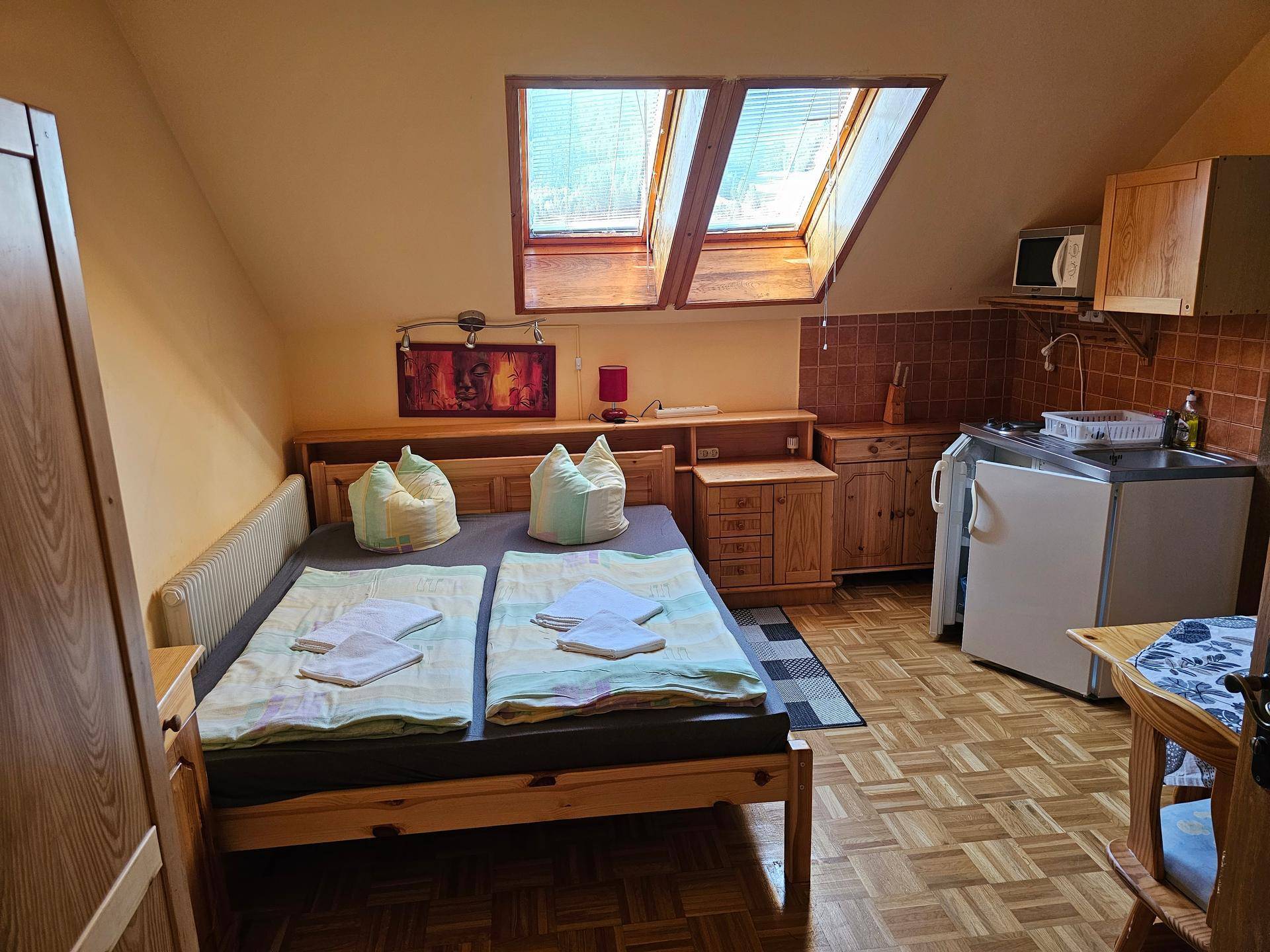 Schlafzimmer mit Doppelbett, Holzmöbeln, kleiner Küchenzeile und zwei Dachfenstern für viel Licht.