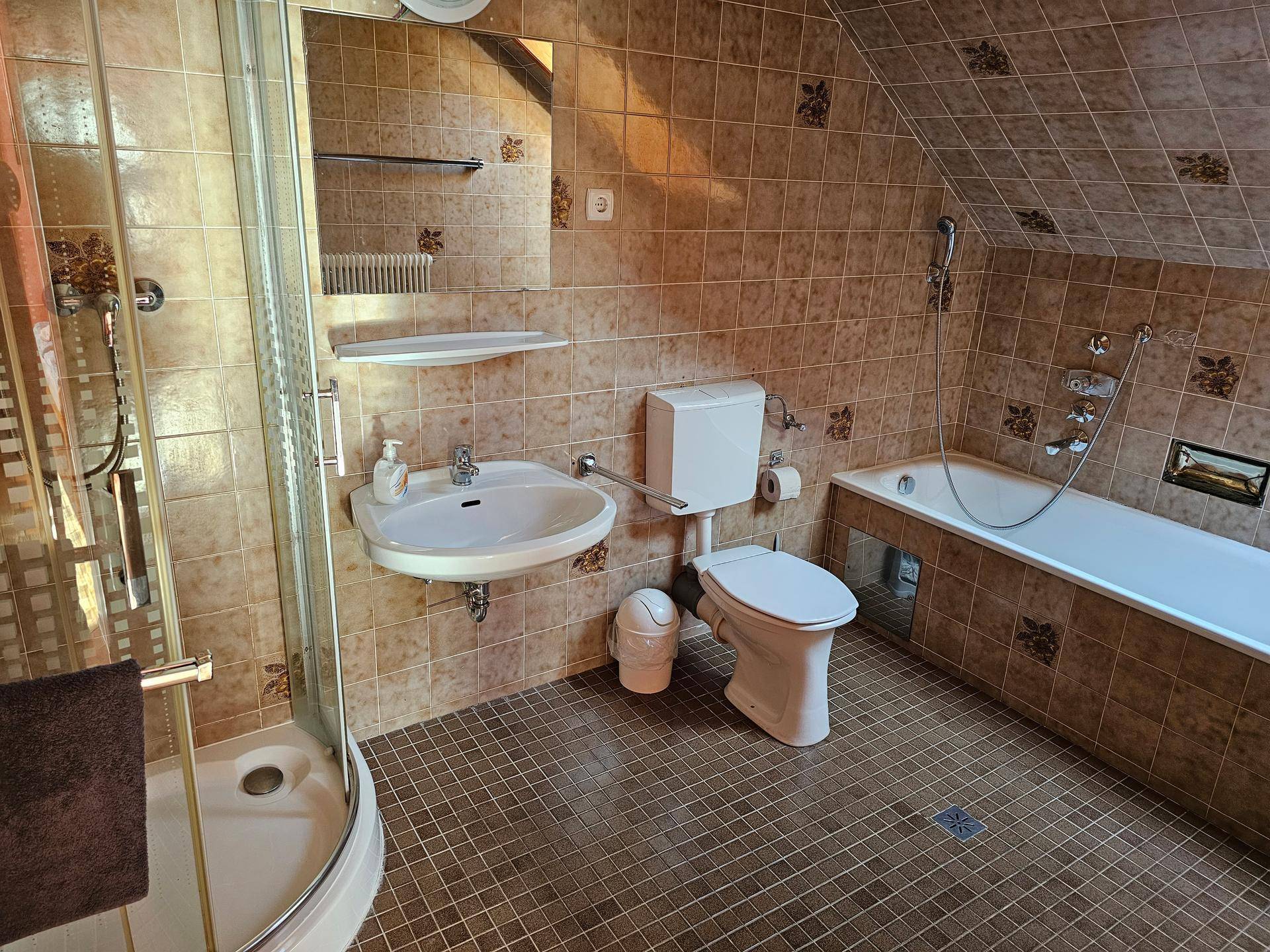 Badezimmer mit Dusche, Badewanne, WC und Waschbecken, komplett gefliest und mit Dachschräge.