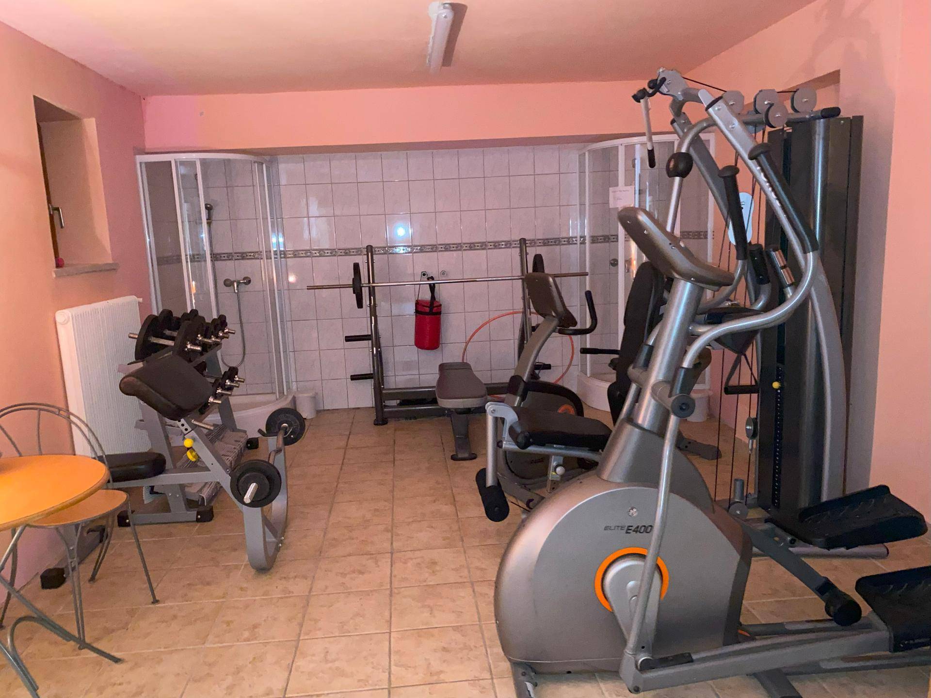 Fitnessraum mit verschiedenen Trainingsgeräten, einem Boxsack und zwei Duschkabinen.