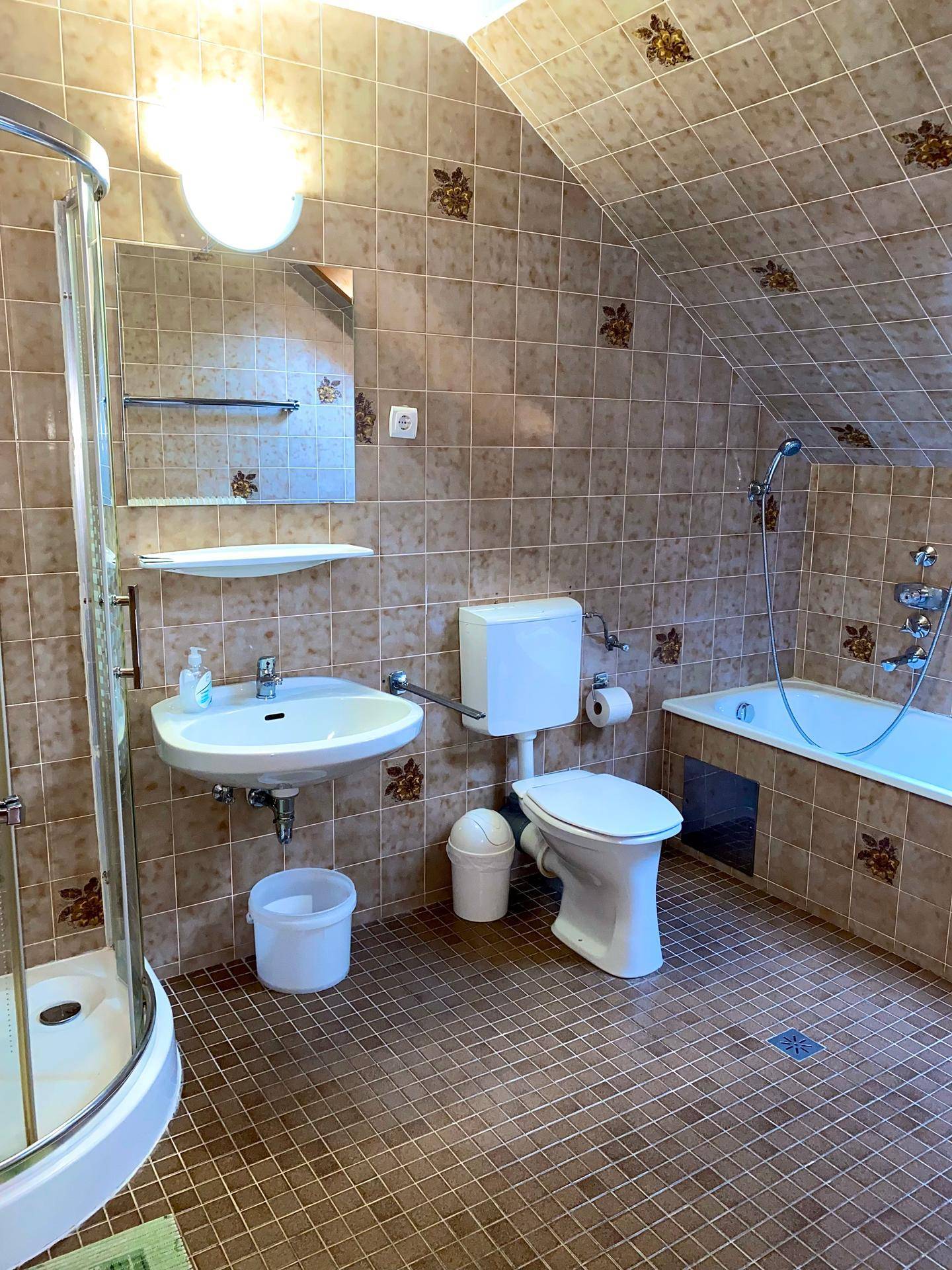 Badezimmer mit Duschkabine, Waschbecken, Toilette und Spiegel, vollständig gefliest.