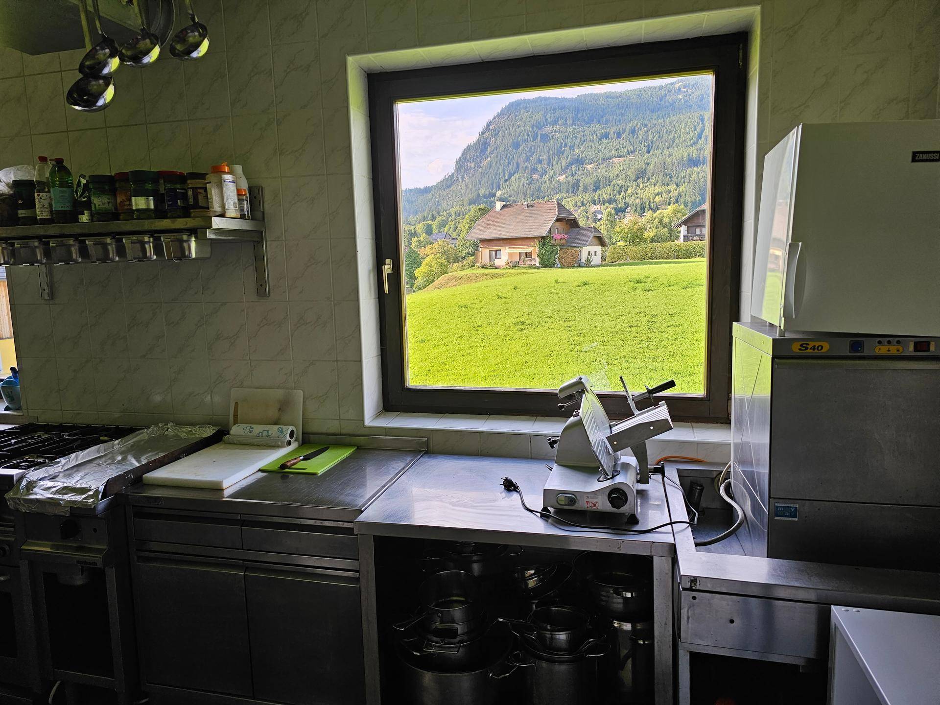 Industrielle Küche mit Edelstahloberflächen und einem Fenster mit Blick auf ein Haus im Grünen.