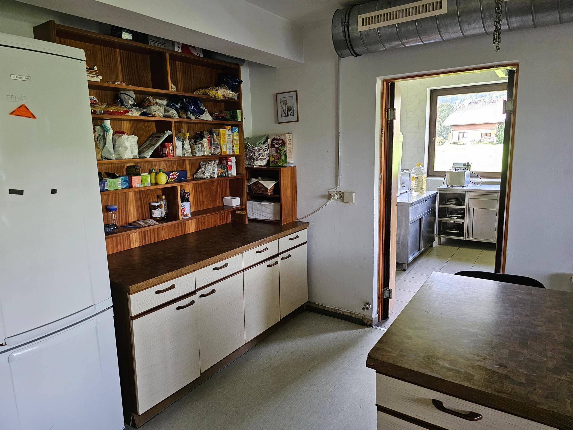 Küche oder Speisekammer mit offenen Regalen, Schränken, Kühlschrank und Fenster mit Blick ins Grüne.