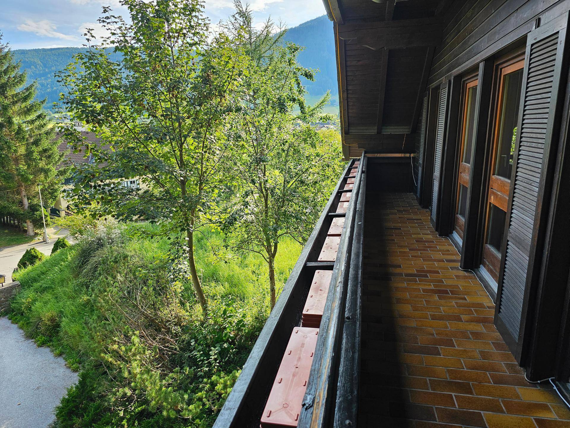 Langer, schmaler Balkon mit Ziegelboden und Blick auf grüne Bäume und die umliegende Landschaft.