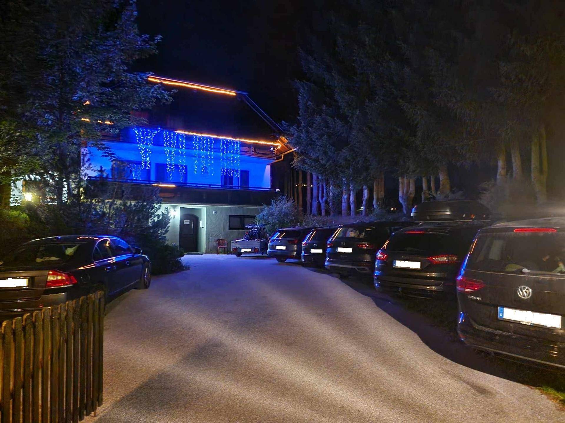 Gebäude bei Nacht mit festlicher blauer und oranger Beleuchtung und geparkten Autos auf dem Vorplatz.