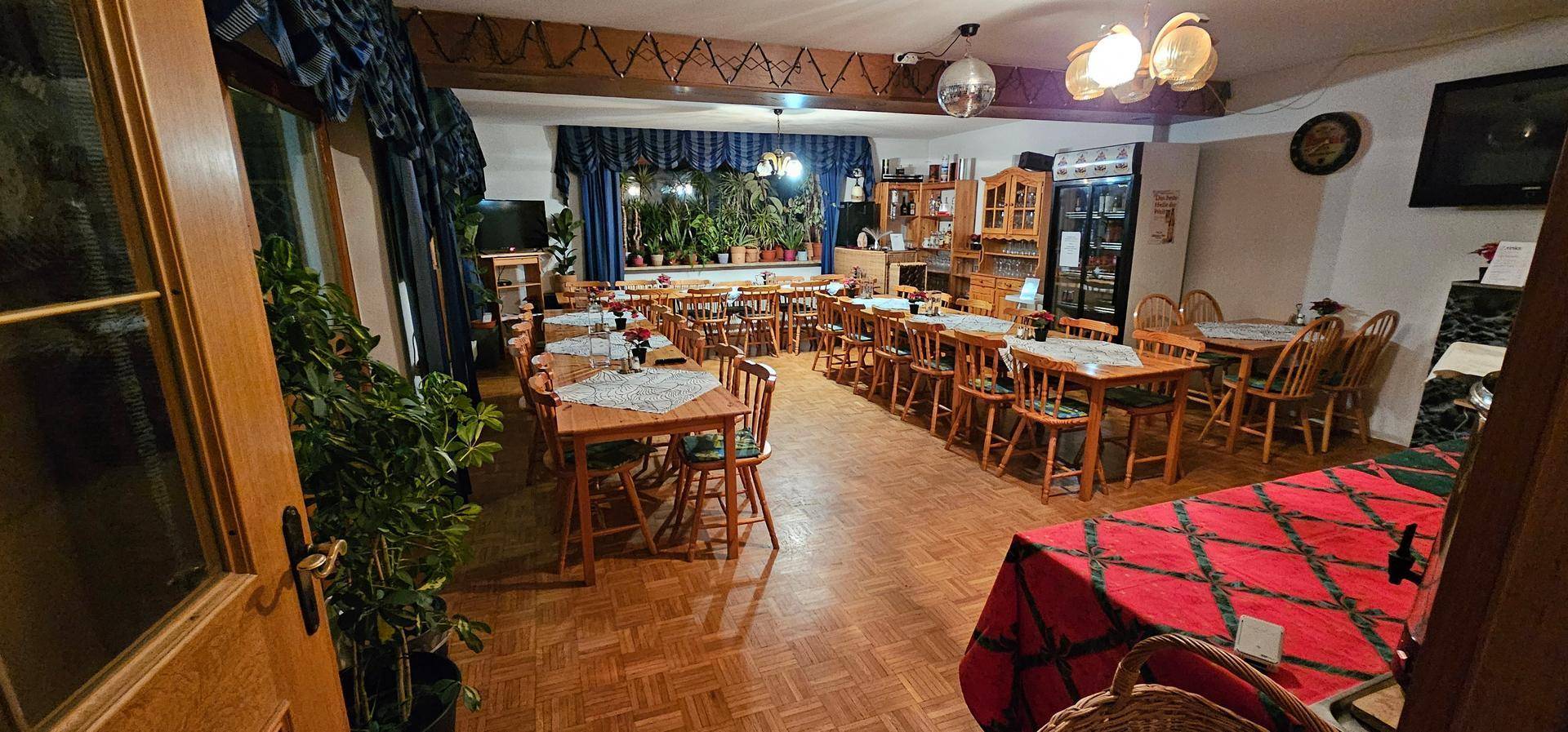Geräumiger Speisesaal mit vielen Holztischen und Stühlen, Parkettboden und Pflanzen als Dekoration.