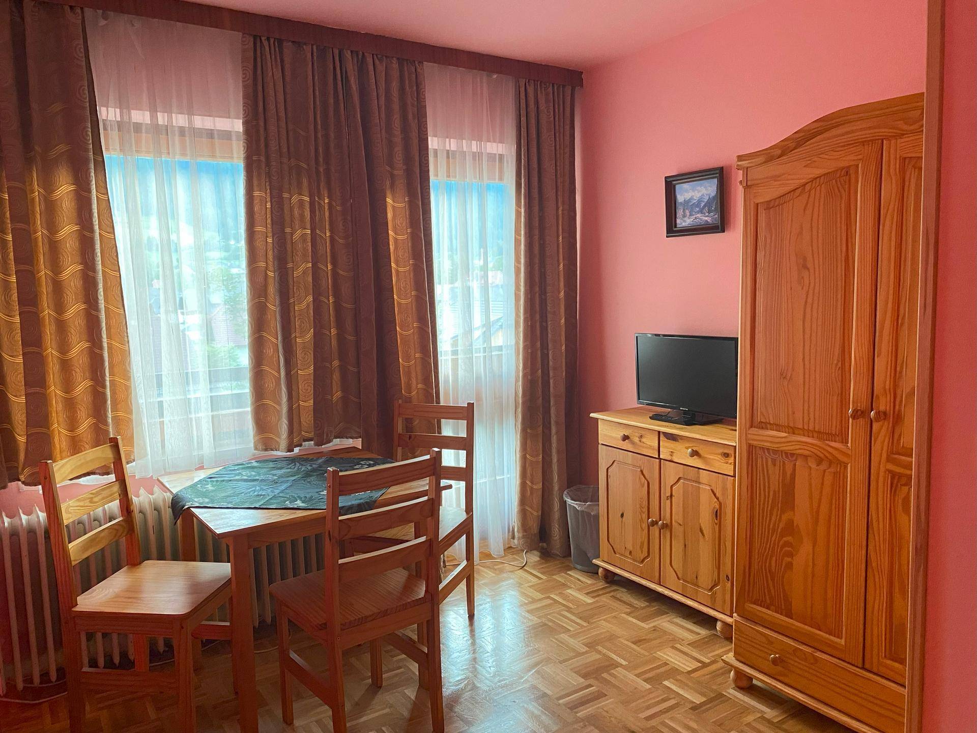 Schlafzimmer mit kleinem Esstisch, Kleiderschrank und Fernseher, in rosa Farbtönen gehalten.