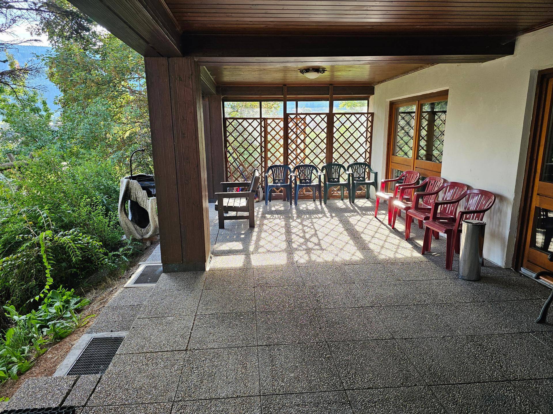 Überdachte Terrasse mit Gartenstühlen und einem Ausblick ins Grüne.