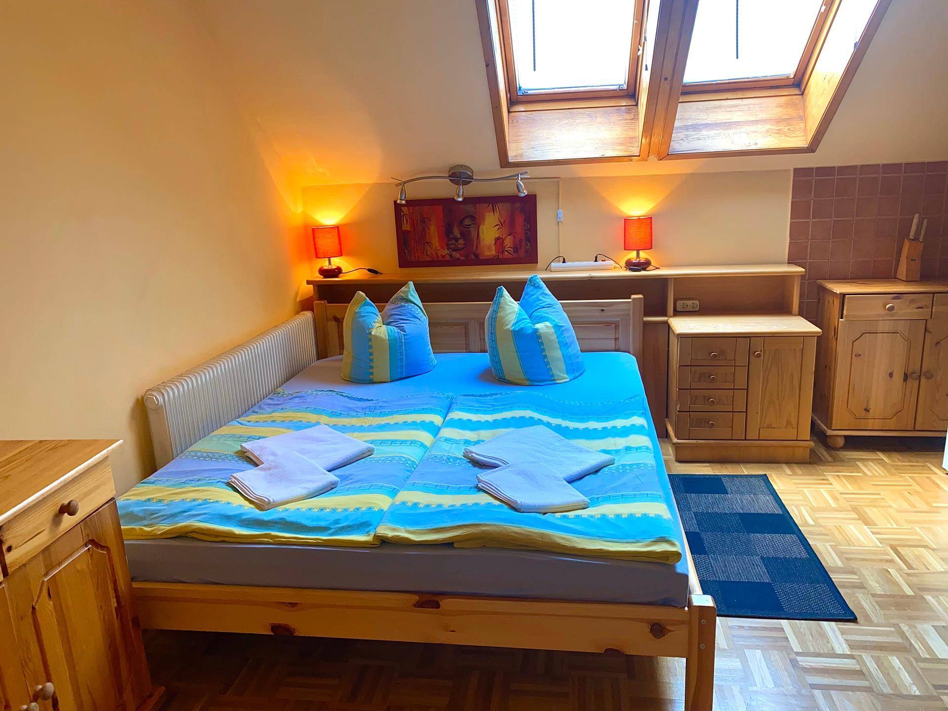 Studio-Apartment mit Doppelbett, Küchenzeile und zwei Dachfenstern, die den Raum erhellen.
