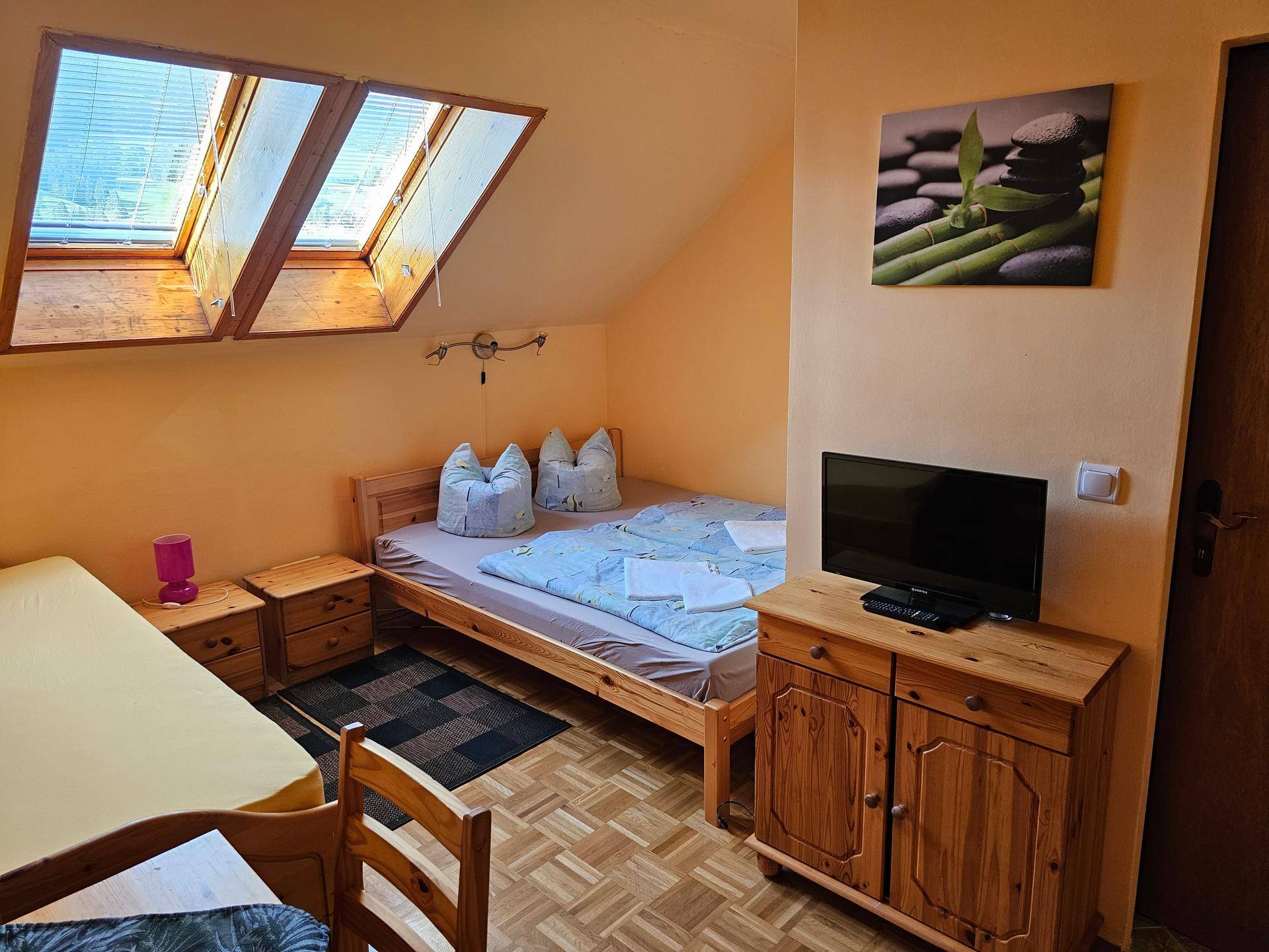 Schlafzimmer mit zwei Einzelbetten, Holzboden und Dachfenstern, die viel natürliches Licht hereinlassen.
