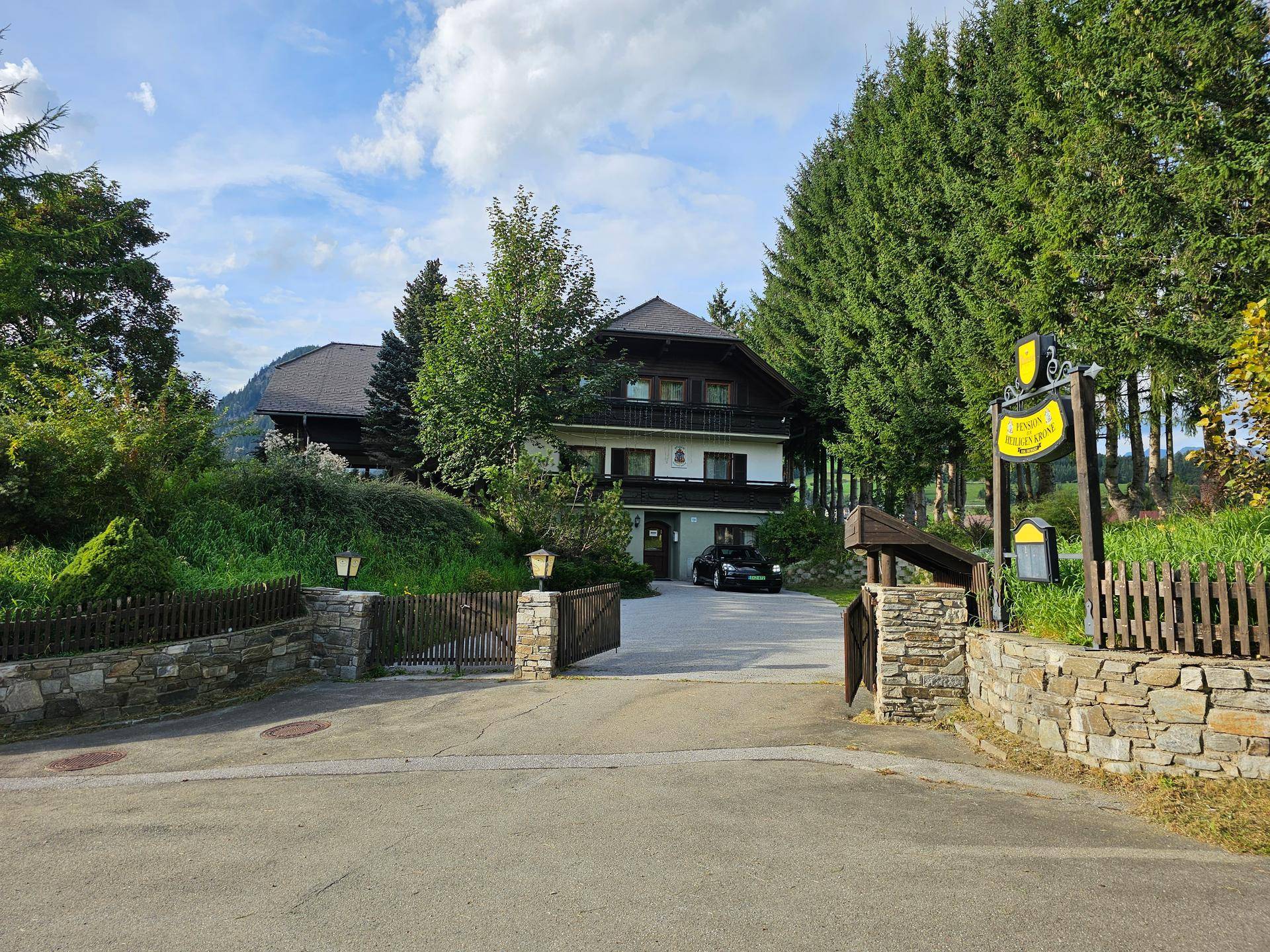 Traditionelles Haus mit gepflegter Zufahrt, Steinfassaden und umgebenden Nadelbäumen in bergiger Landschaft.