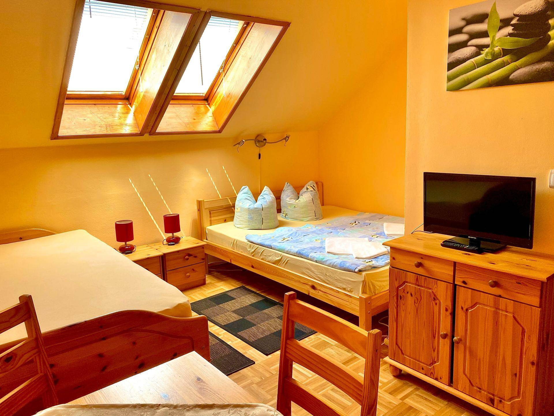 Studio-Apartment mit zwei Einzelbetten, kleinem Tisch und zwei Dachfenstern für helles Tageslicht.