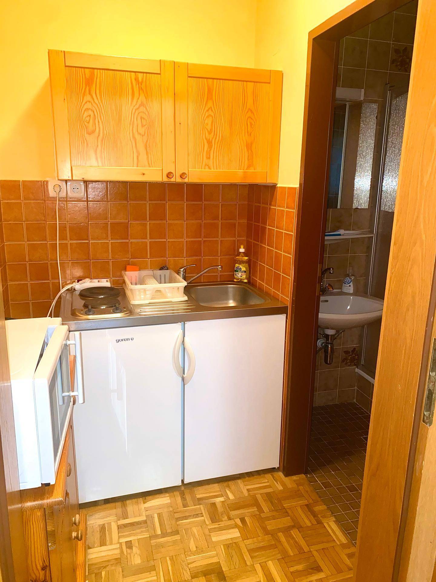 Kleine Küchenzeile mit Spüle, Herd, Mikrowelle und Kühlschrank, angrenzend an ein Badezimmer.