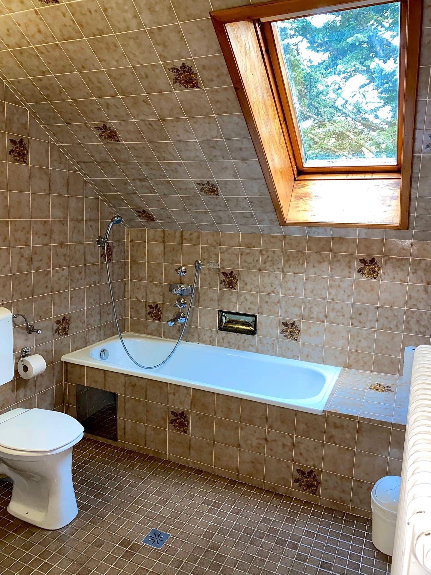 Badezimmer mit Badewanne, Toilette und einem Dachfenster, komplett gefliest.