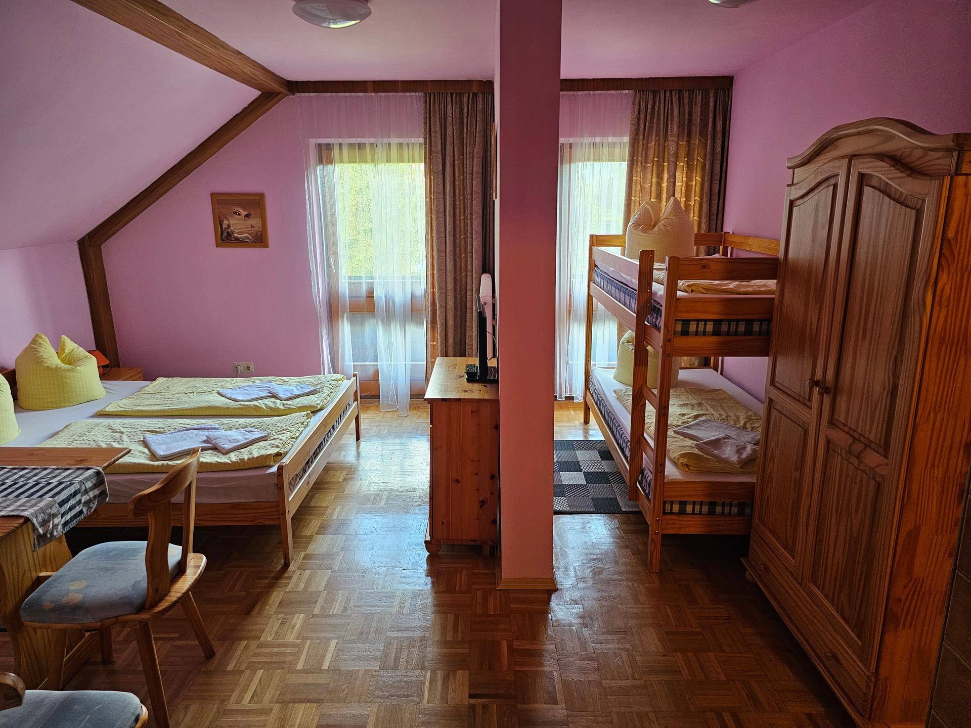 Schlafzimmer mit Doppelbett, Etagenbett und Kleiderschrank, rosa Wände und Holzboden.