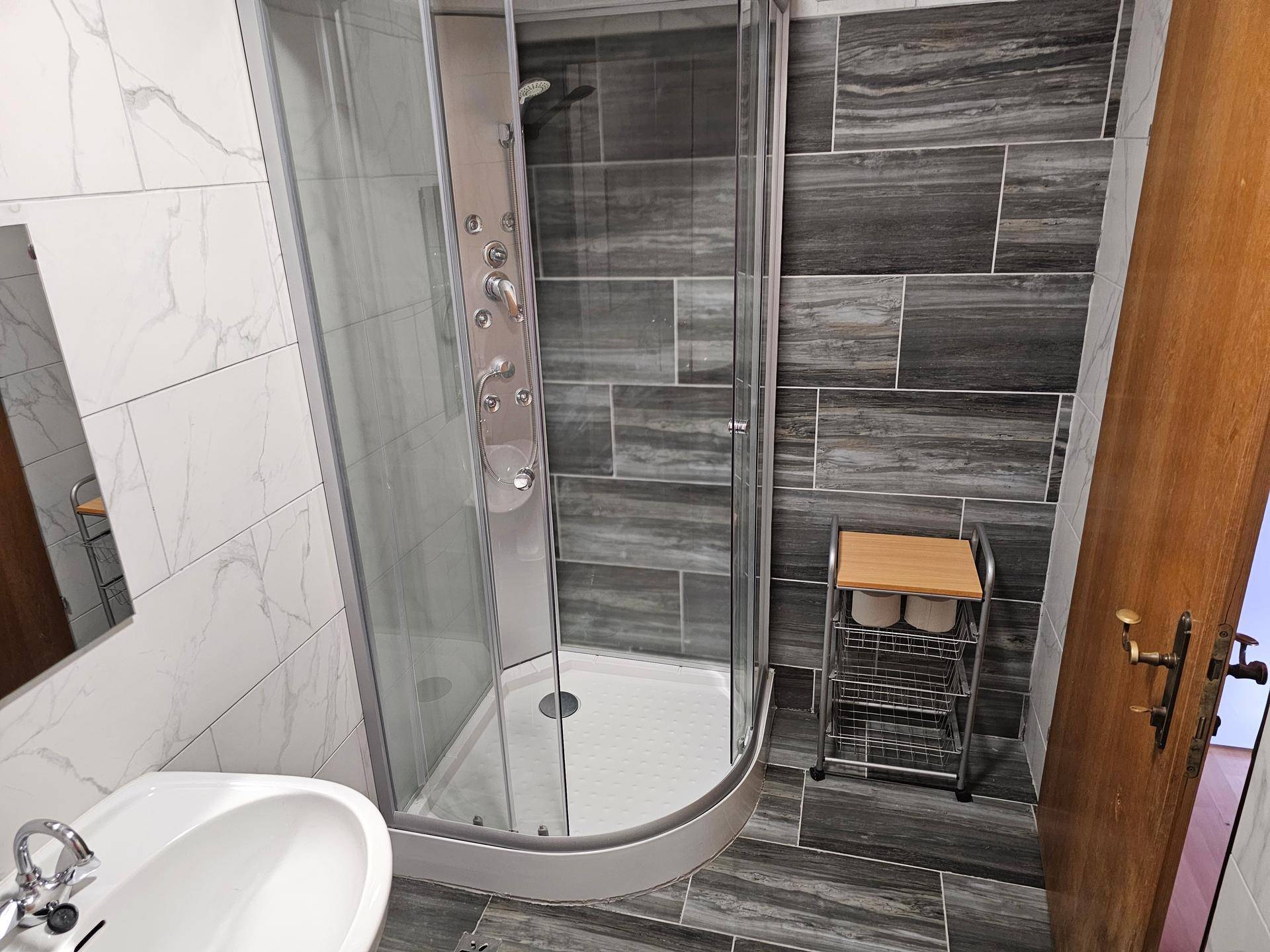 Modernes Badezimmer mit Eckdusche, Waschbecken und einer Kombination aus hellen und dunklen Fliesen.