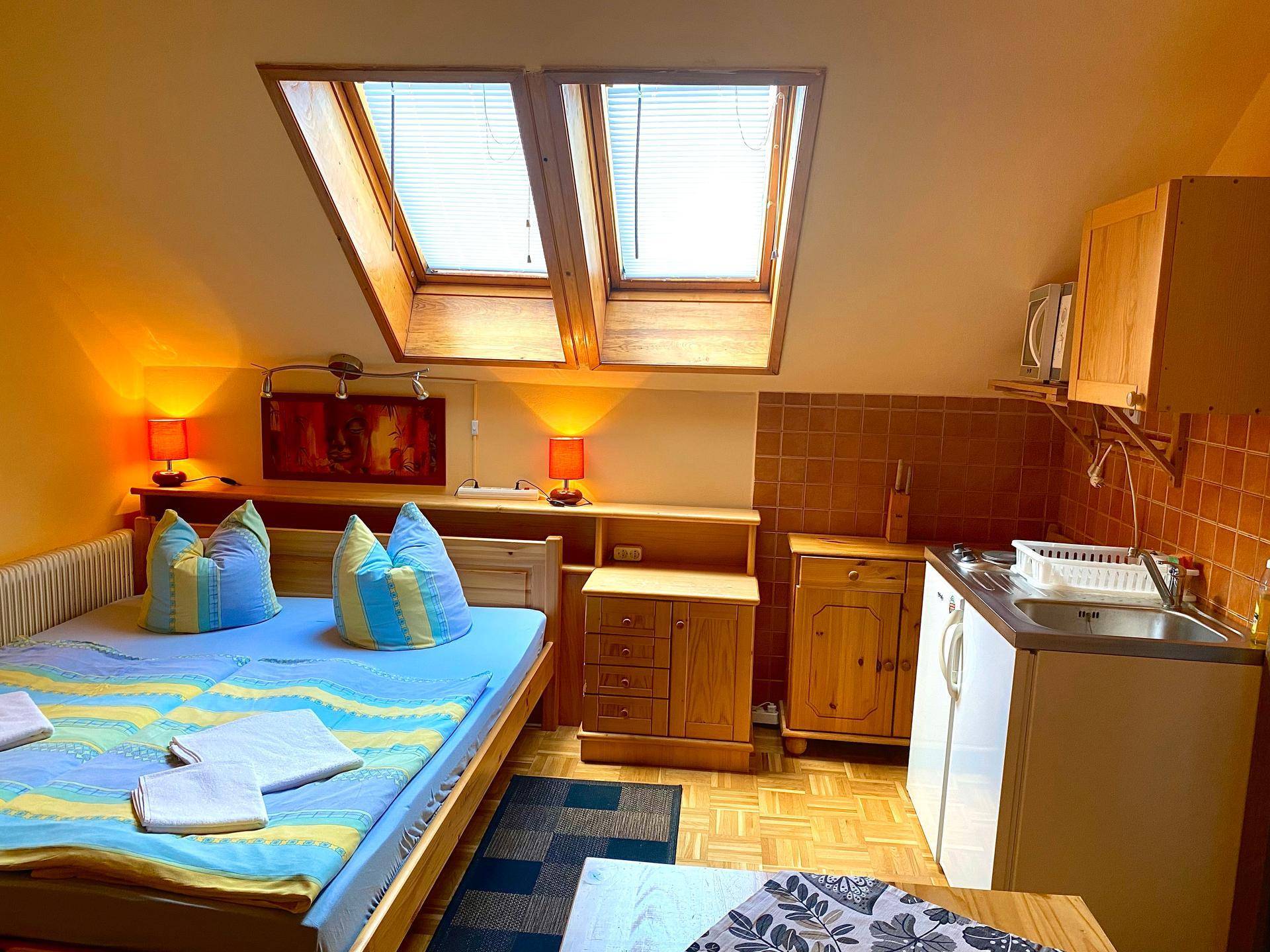Studio-Apartment mit Doppelbett, Küchenzeile und zwei Dachfenstern, die viel Licht hereinlassen.