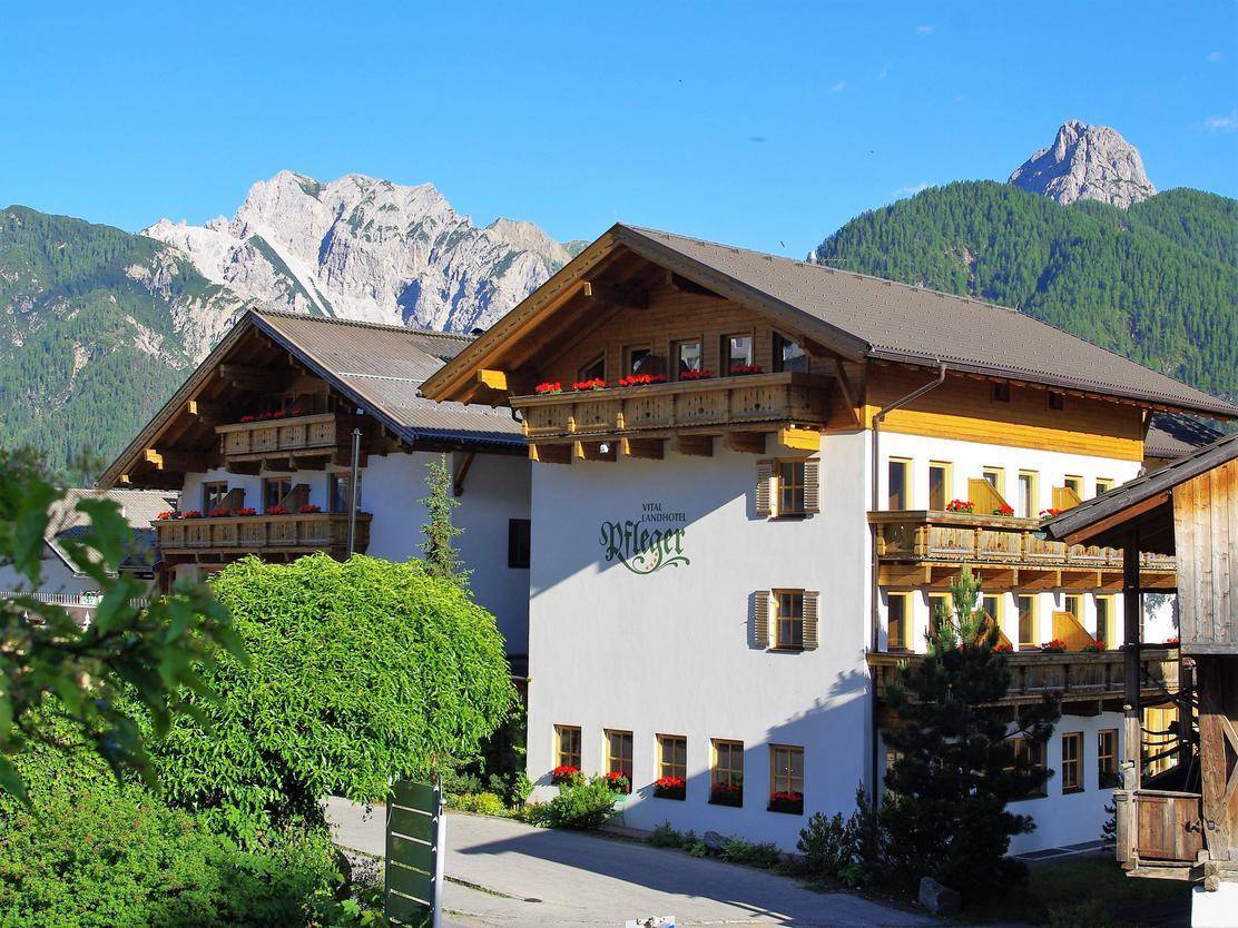 Traditionelles alpines Gebäude mit Holzbalkonen und Blumenkästen vor einer beeindruckenden Bergkulisse.