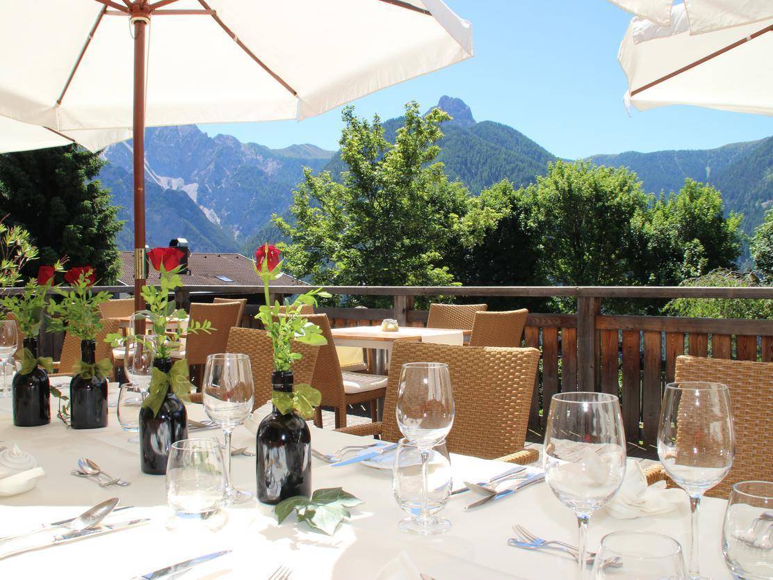 Sonnige Außenterrasse mit Tischen, Stühlen und Sonnenschirmen, die einen weiten Blick auf die Berge bietet.