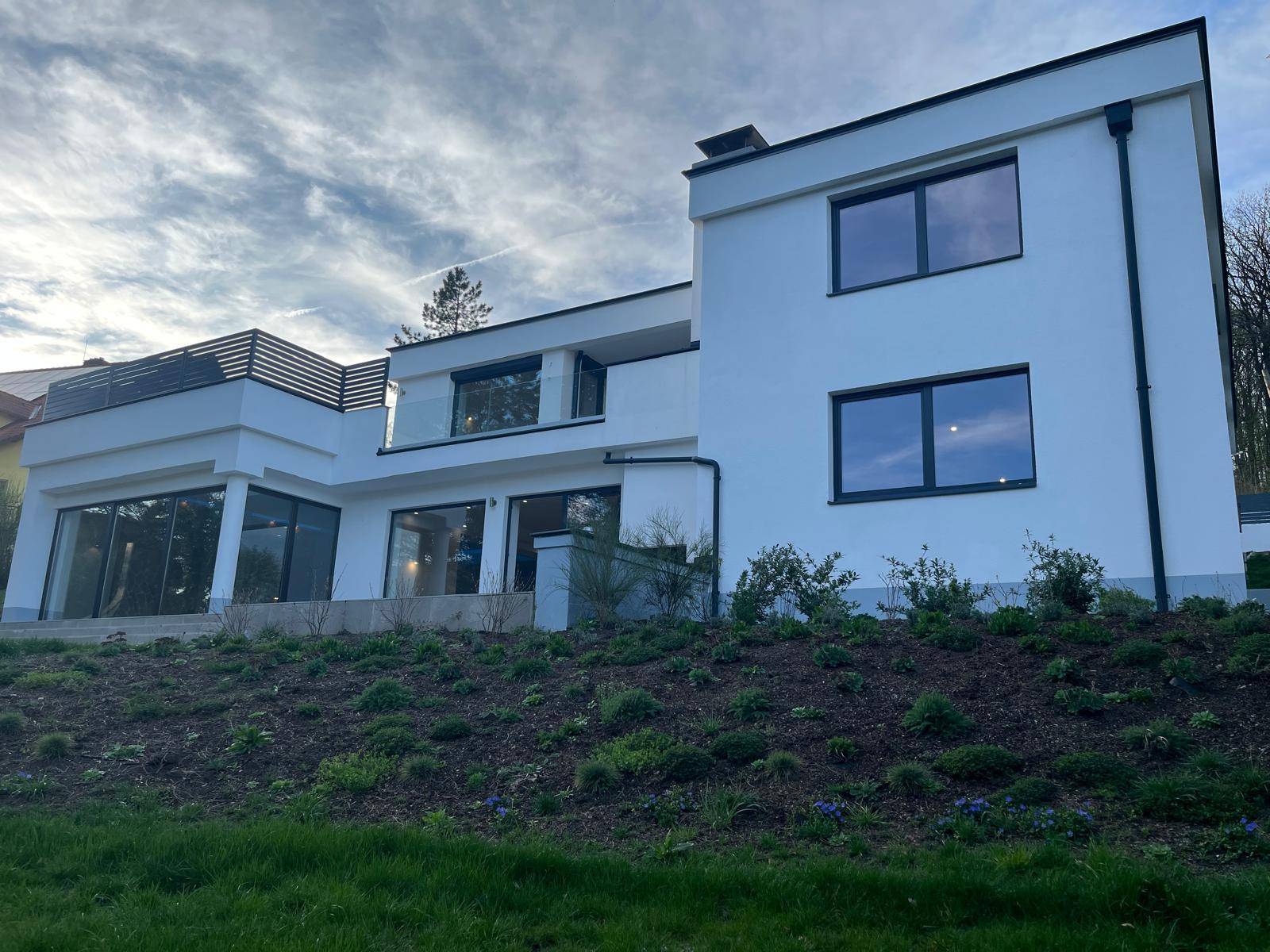 Moderne Villa mit weißer Fassade, großen Fenstern und terrassiertem Gartenbereich.