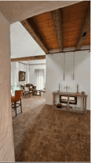 Offener Wohnbereich mit Kamin, Holzbalken und rustikalem Ziegelboden, lichtdurchflutet.