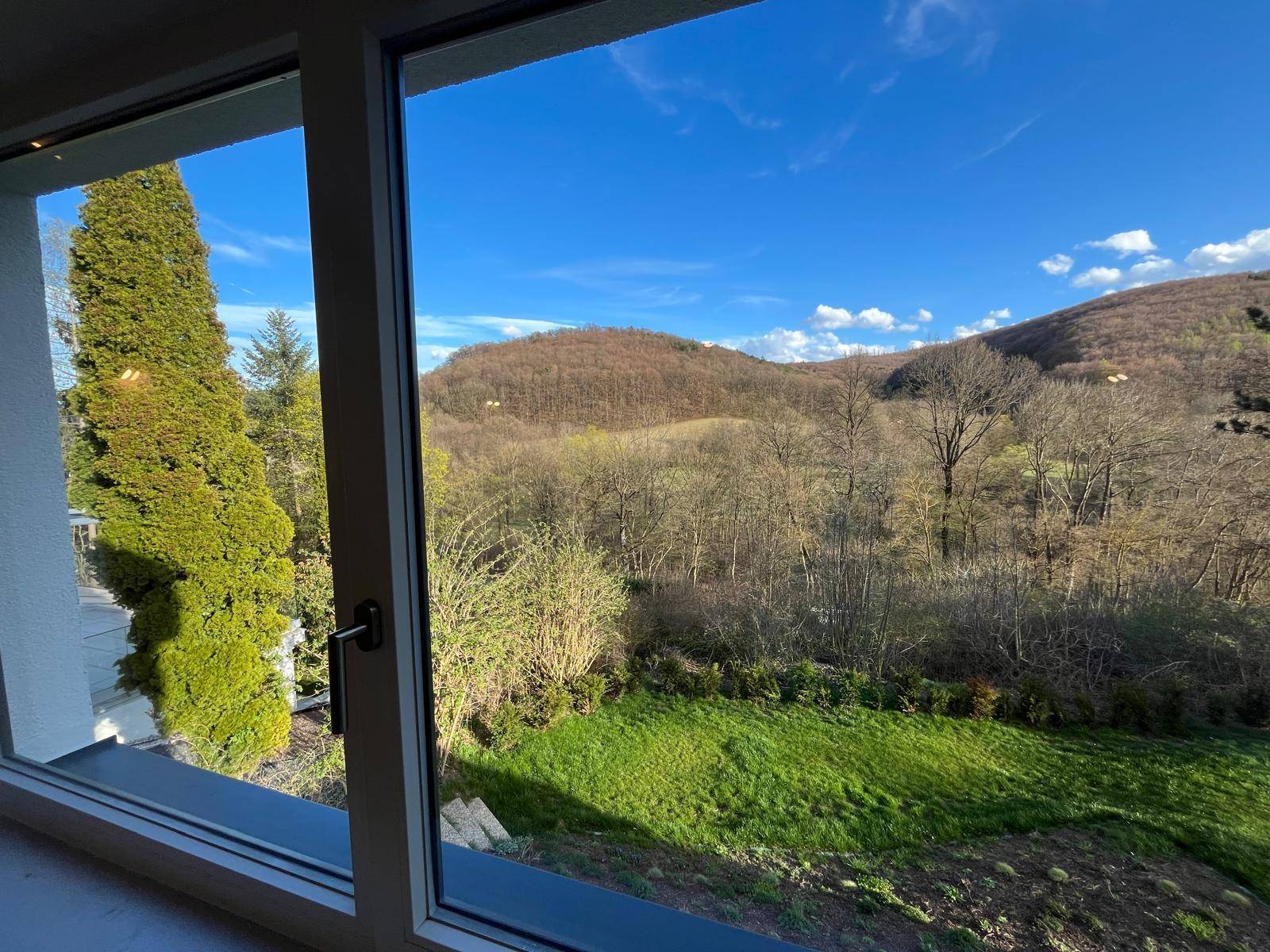 Heller Innenraum mit großem Fenster und weitem Blick auf die grüne Hügellandschaft.