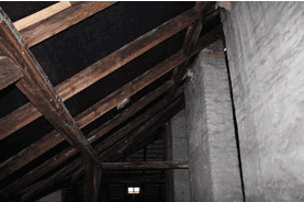 Detailansicht des Dachstuhls mit Holzbalken und einer massiven Säule im ungenutzten Dachboden.