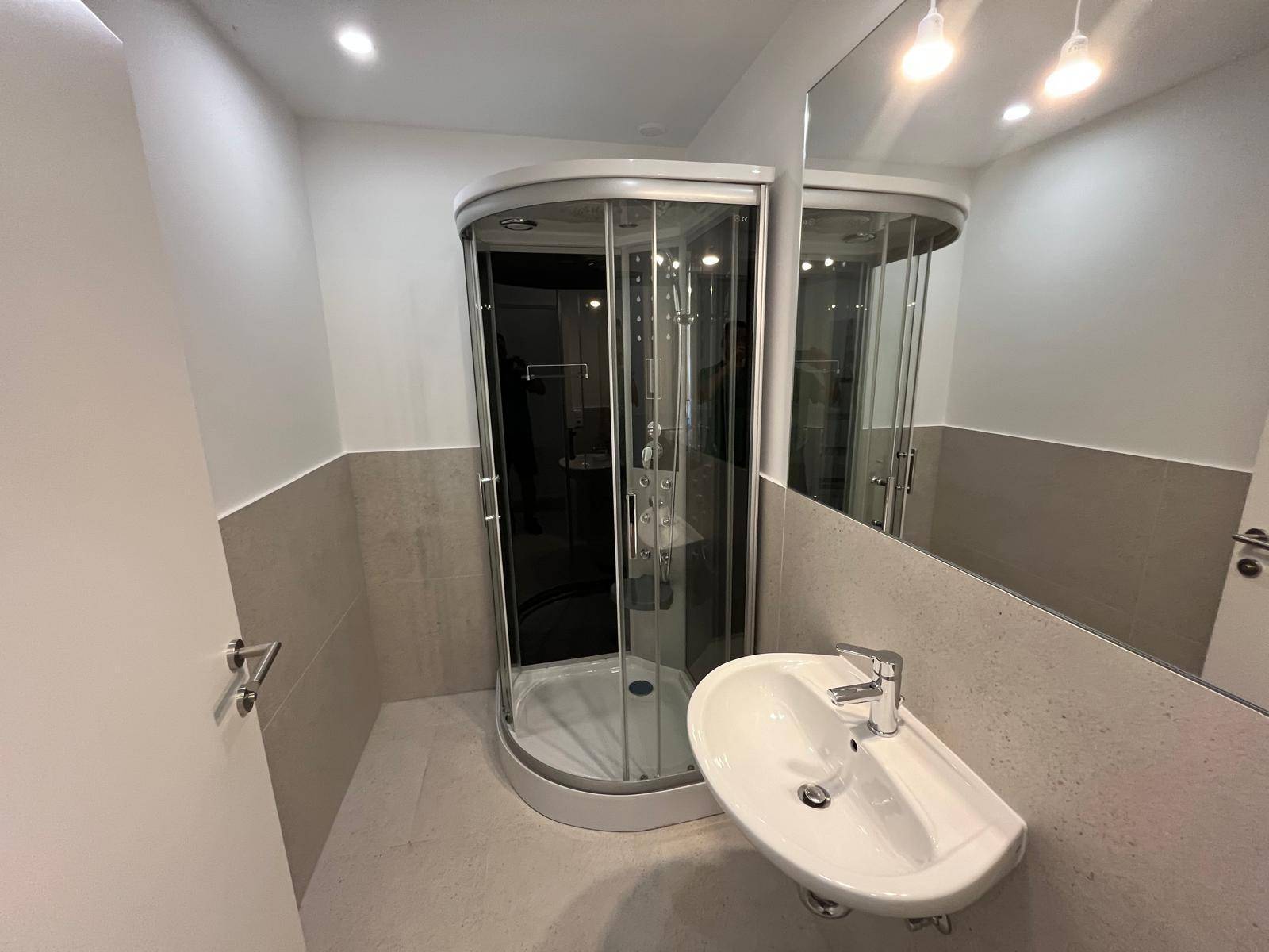 Modernes Badezimmer mit Duschkabine, Waschbecken und großem Spiegel.