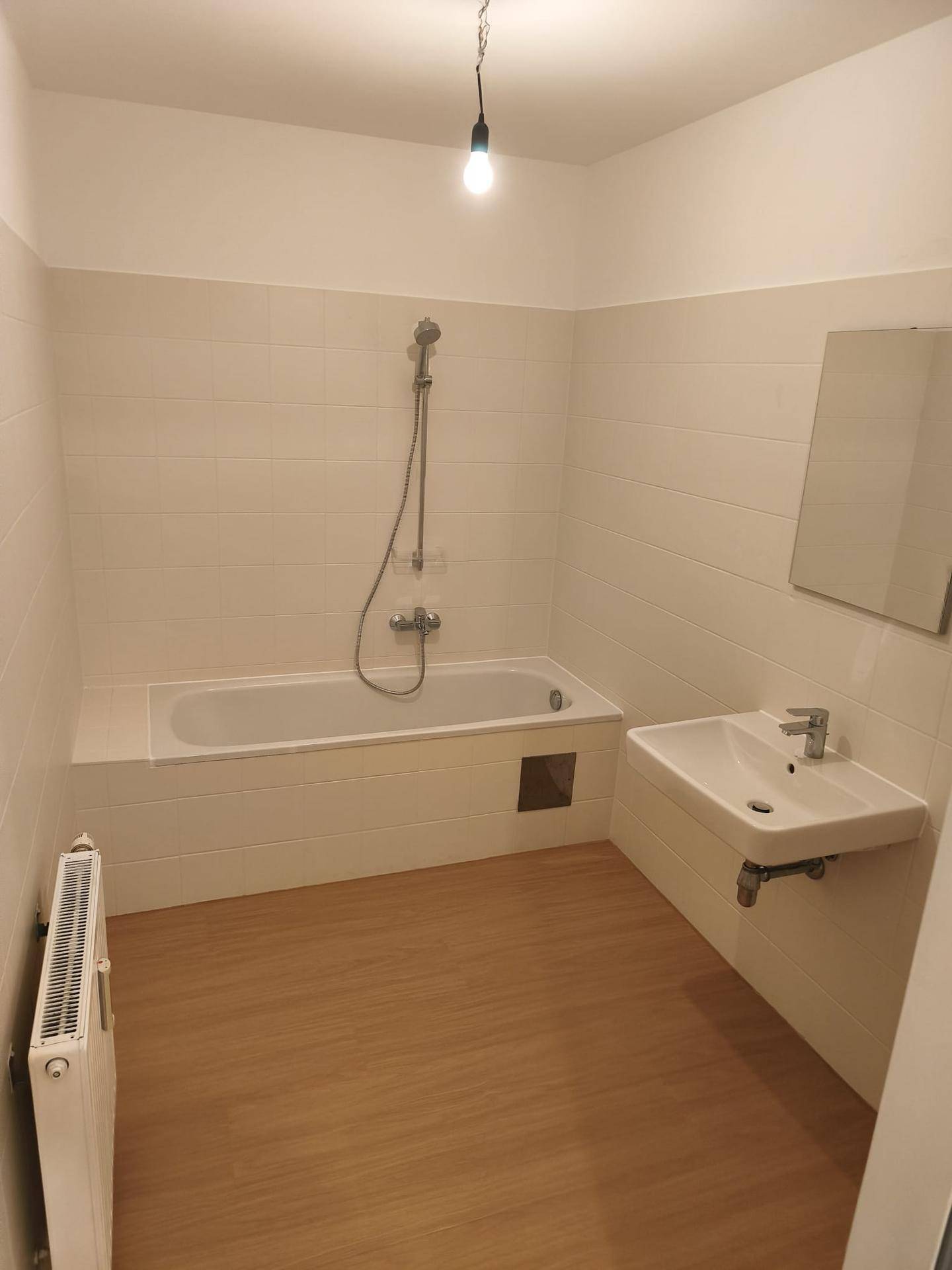 Badezimmer mit Badewanne, Waschbecken und weißen Fliesen, ausgestattet mit Heizkörper.
