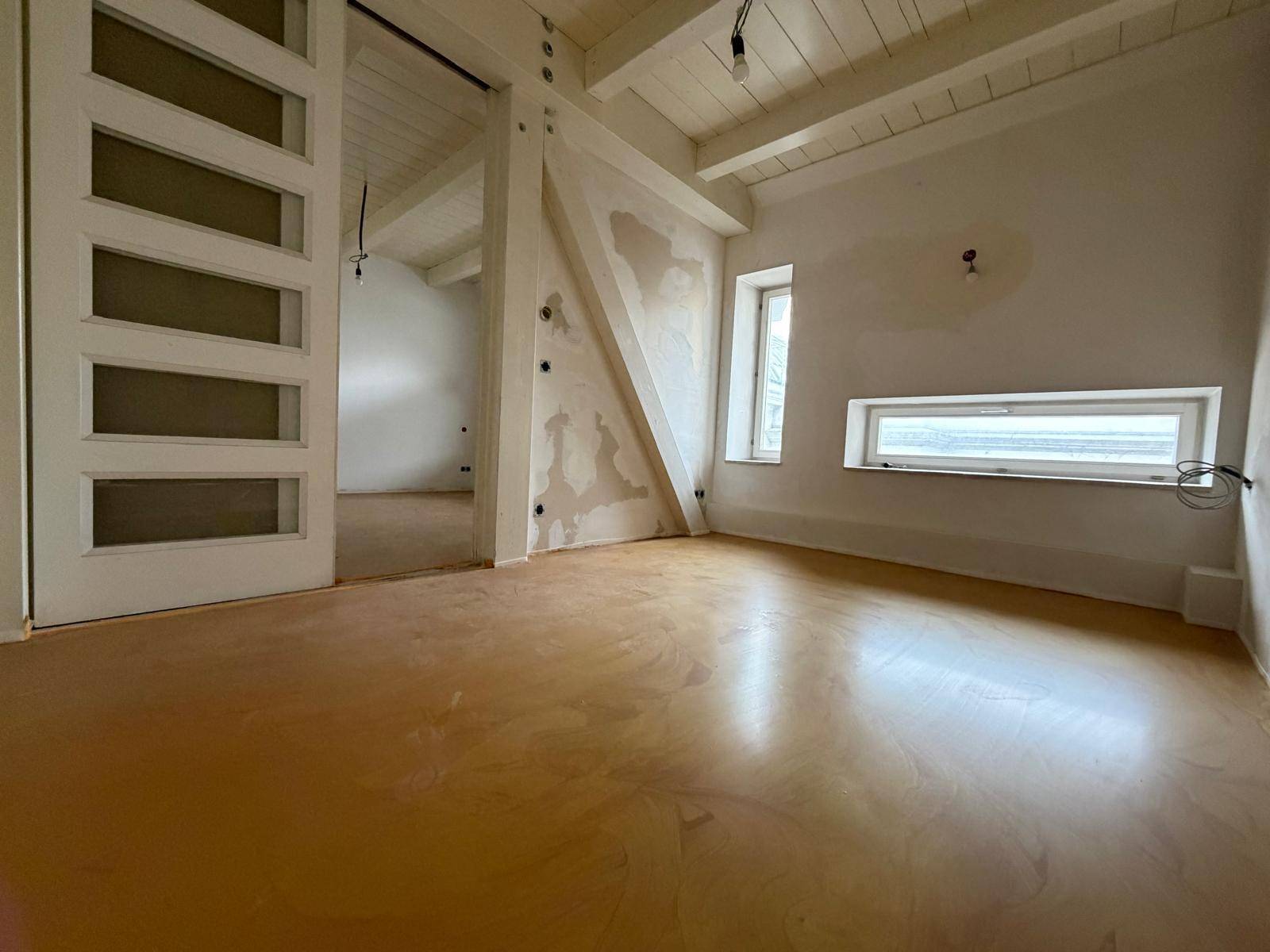 Raum im Bau mit gelbem Boden, weißen Wänden und kleinen, schmalen Fenstern.