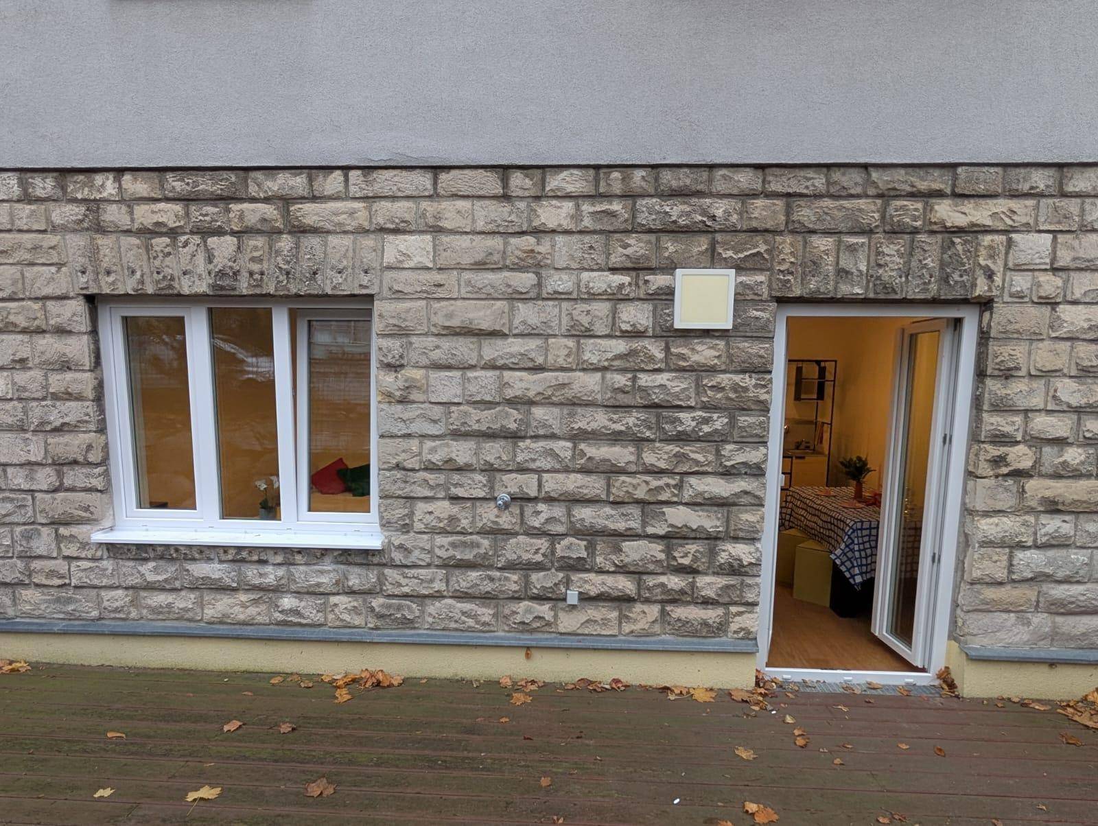 Außenansicht der Steinfassade mit Fenster und Zugang zur Terrasse und dem Innenbereich.