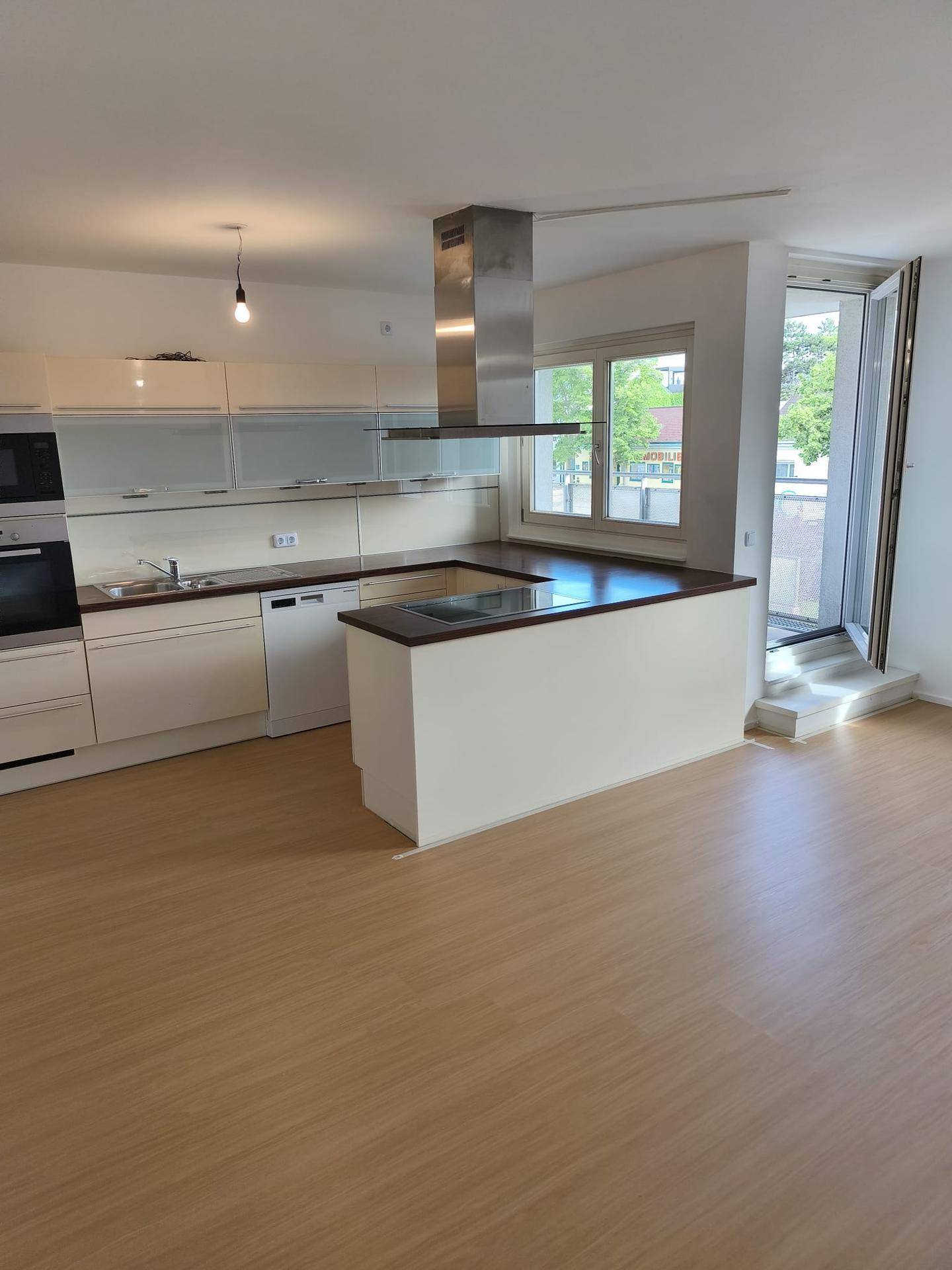 Moderne offene Küche mit heller Einbauküche, Kochinsel und Zugang zum Balkon.