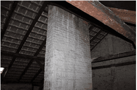 Massive Säule im Dachbodenbereich mit sichtbaren Holzbalken und Dachziegeln, bereit für den Ausbau.