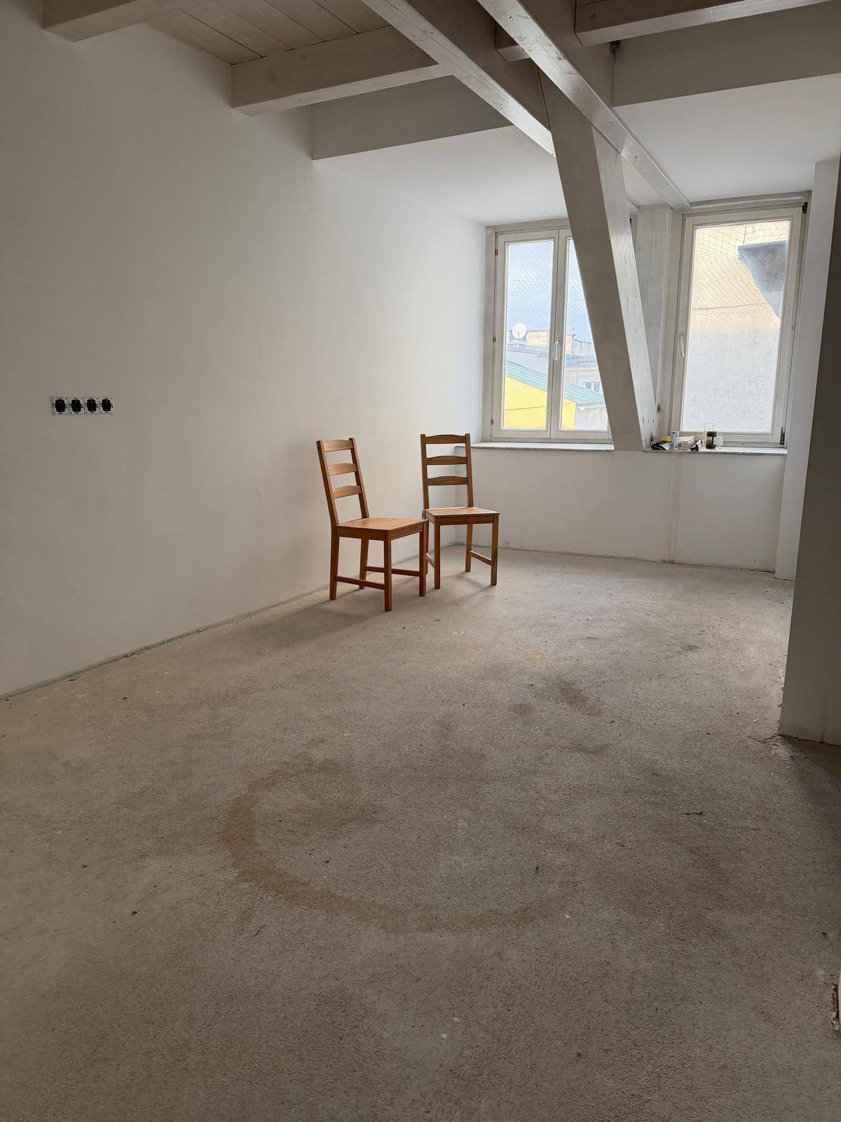 Leerer Raum im Bau mit hohen Decken, Holzbalken und zwei einfachen Holzstühlen.