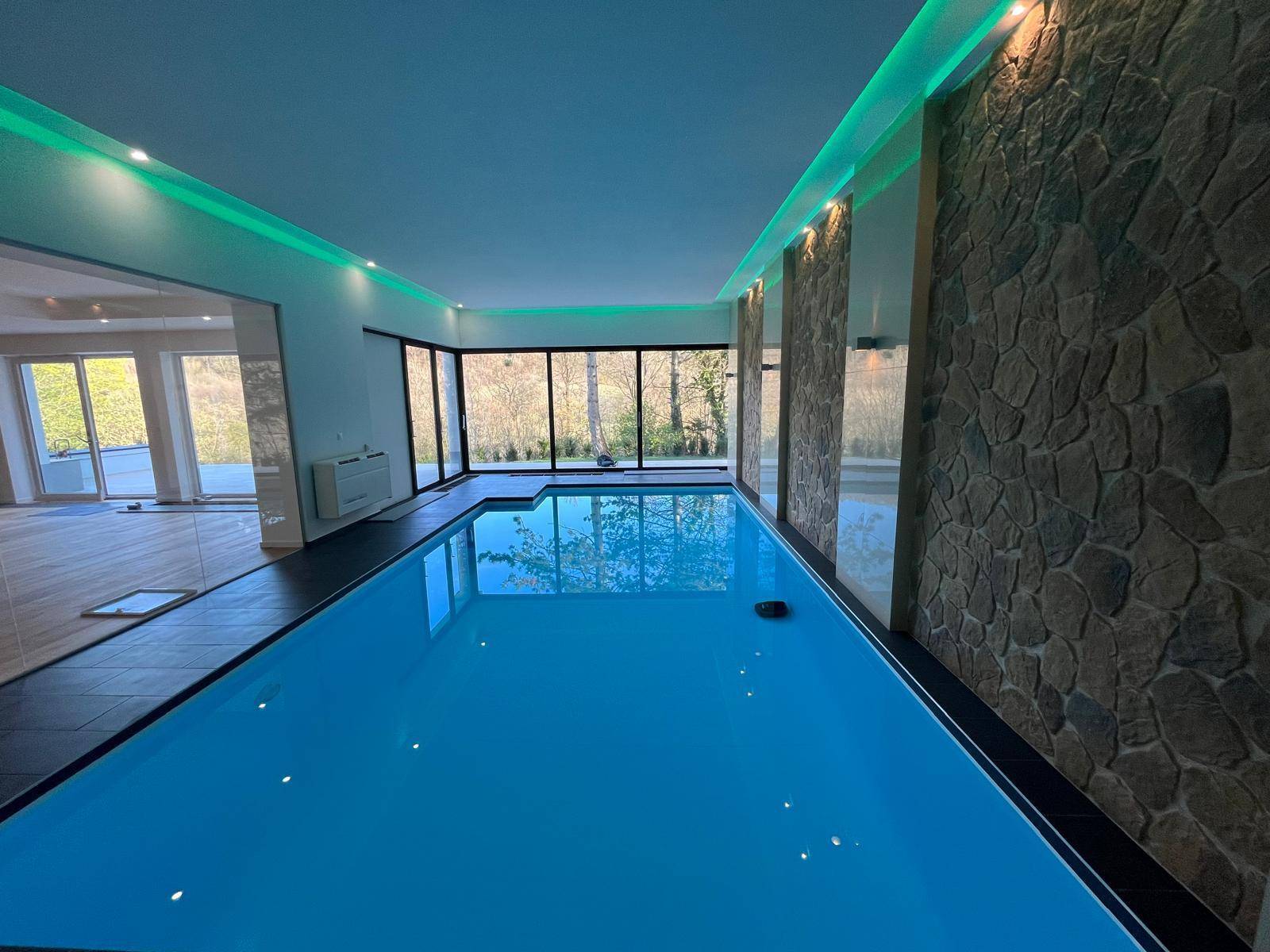 Geräumiger Innenpool mit blauer Beleuchtung und Steinakzenten an den Wänden.