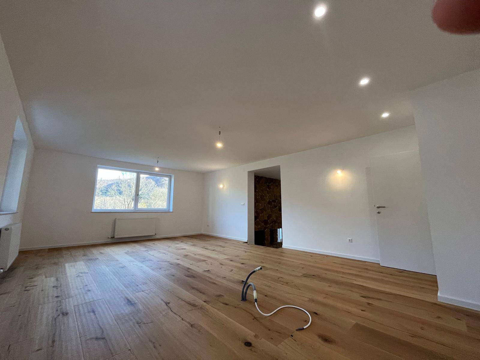 Geräumiges Wohnzimmer mit hellem Holzparkett und Blick auf die grüne Landschaft.