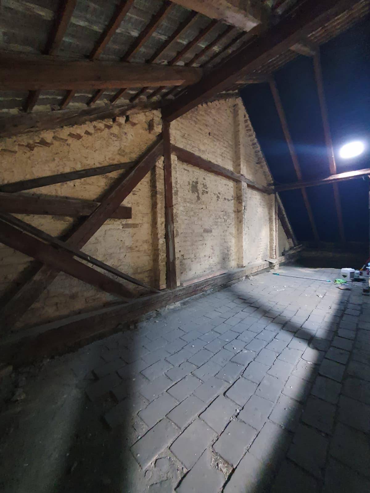 Unausgebauter Dachboden mit freiliegenden Ziegelwänden, Holzbalken und einem Ziegelboden, vielseitig nutzbar.