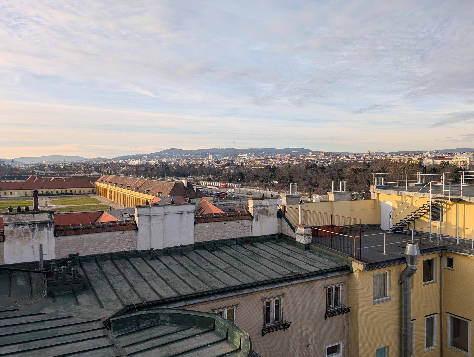 Panoramablick über die Dächer der Stadt, mit einem historischen Schloss in der Ferne und grünen Flächen.