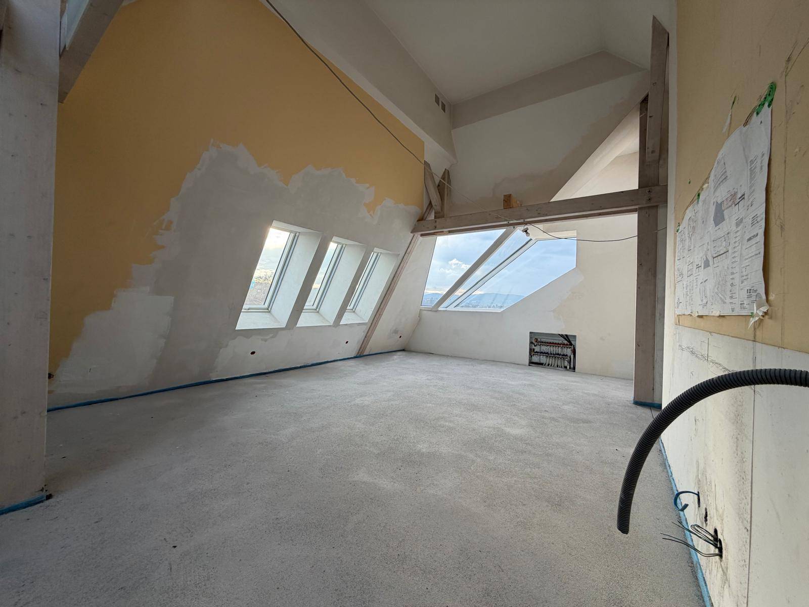 Großer Dachgeschossraum im Bau mit mehreren Dachfenstern, freiliegenden Balken und schrägen Wänden.