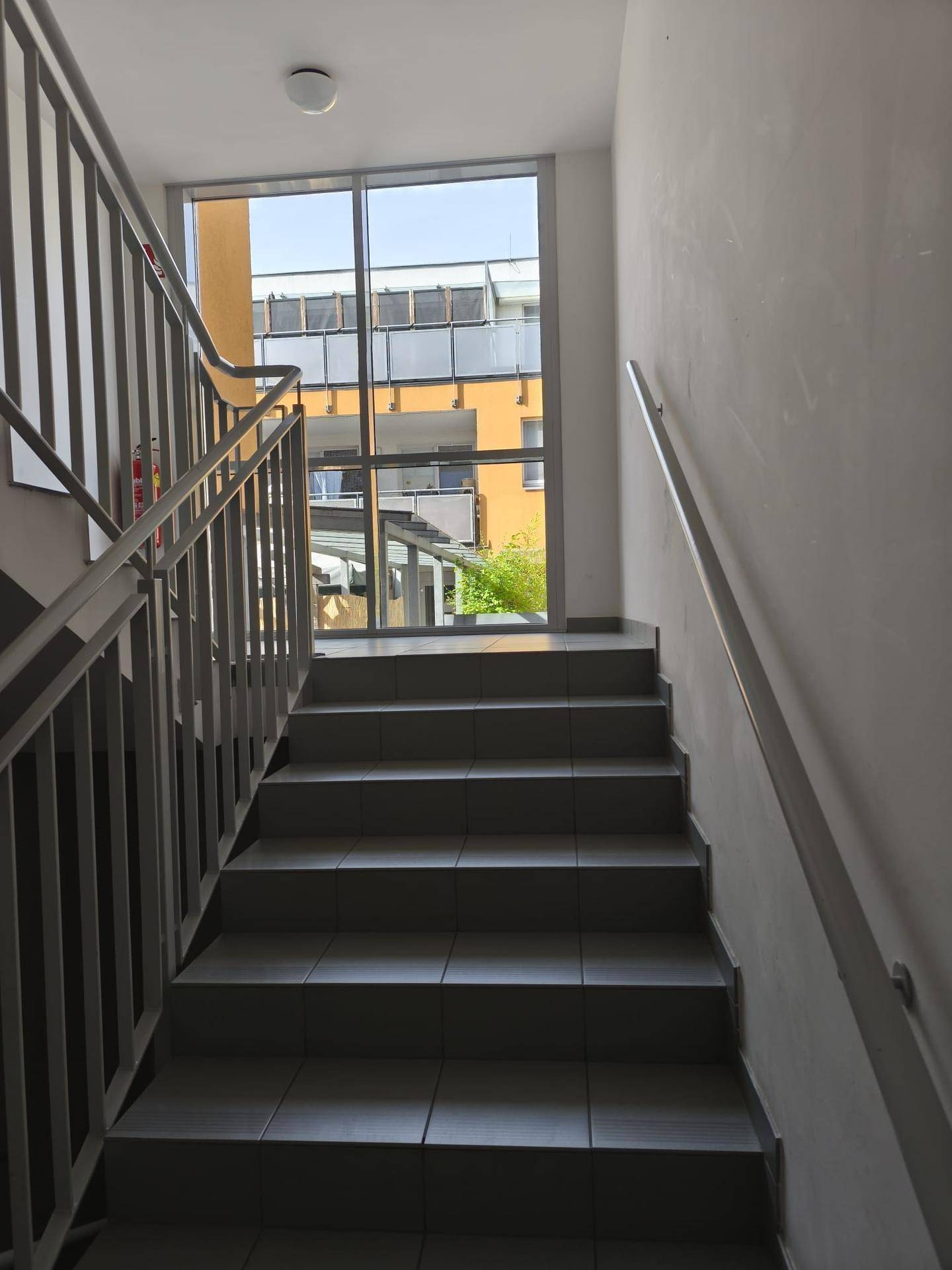 Treppenhaus mit gefliesten Stufen und Metallgeländer, das zu den oberen Etagen führt.