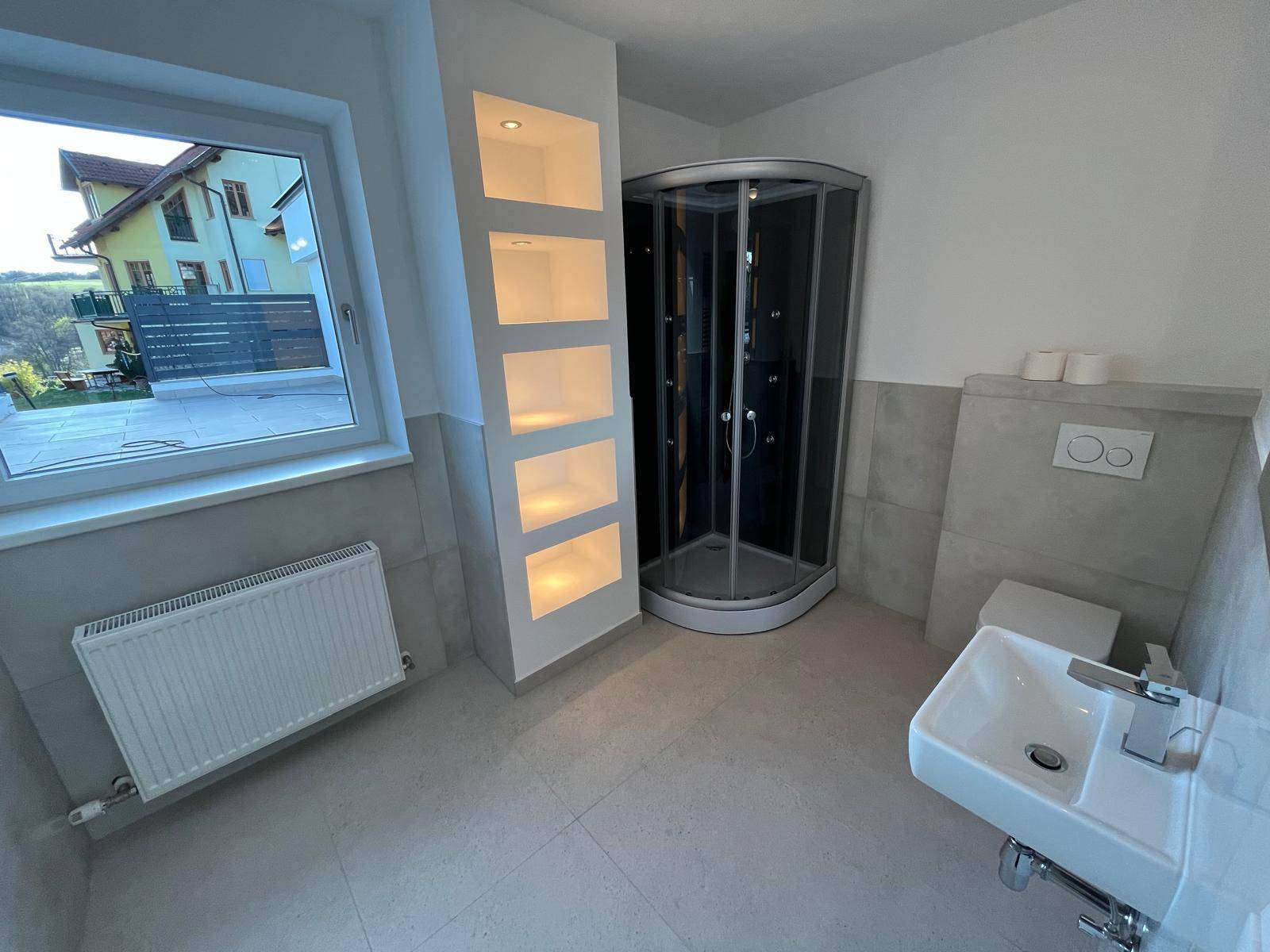 Modernes Badezimmer mit Duschkabine, Waschbecken und beleuchteten Nischen.