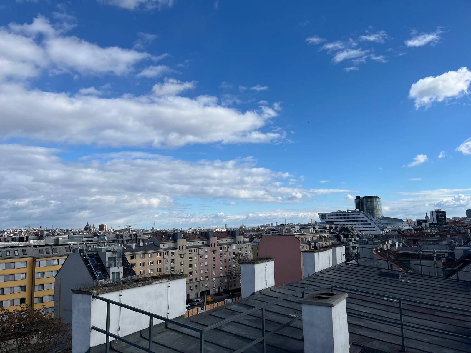 Weitläufiger Blick über die Dächer der Stadt mit blauem Himmel und Wolken.