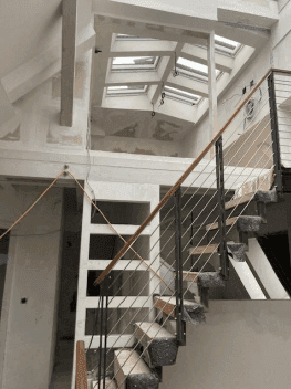 Treppenaufgang in einem im Bau befindlichen Raum mit hohen Decken und vielen Dachfenstern.