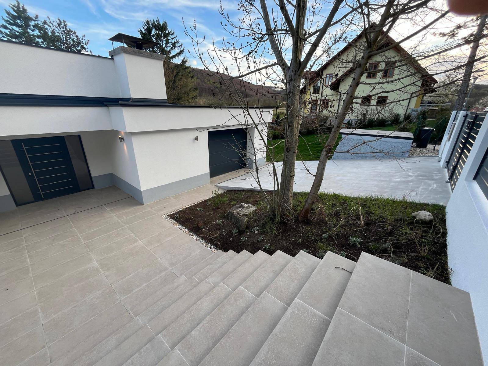 Eingangsbereich der Villa mit gefliestem Vorplatz, Treppe und Garagenzugang.