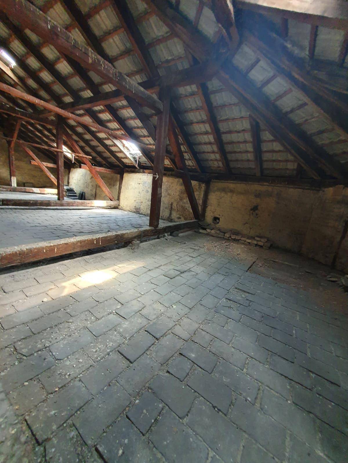 Geräumiger, ungenutzter Dachboden mit sichtbaren Holzbalken und Ziegelboden, bereit für den Ausbau.