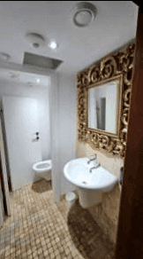 Gäste-WC mit Einzelwaschbecken, WC und opulentem Goldspiegel, komplett gefliest.