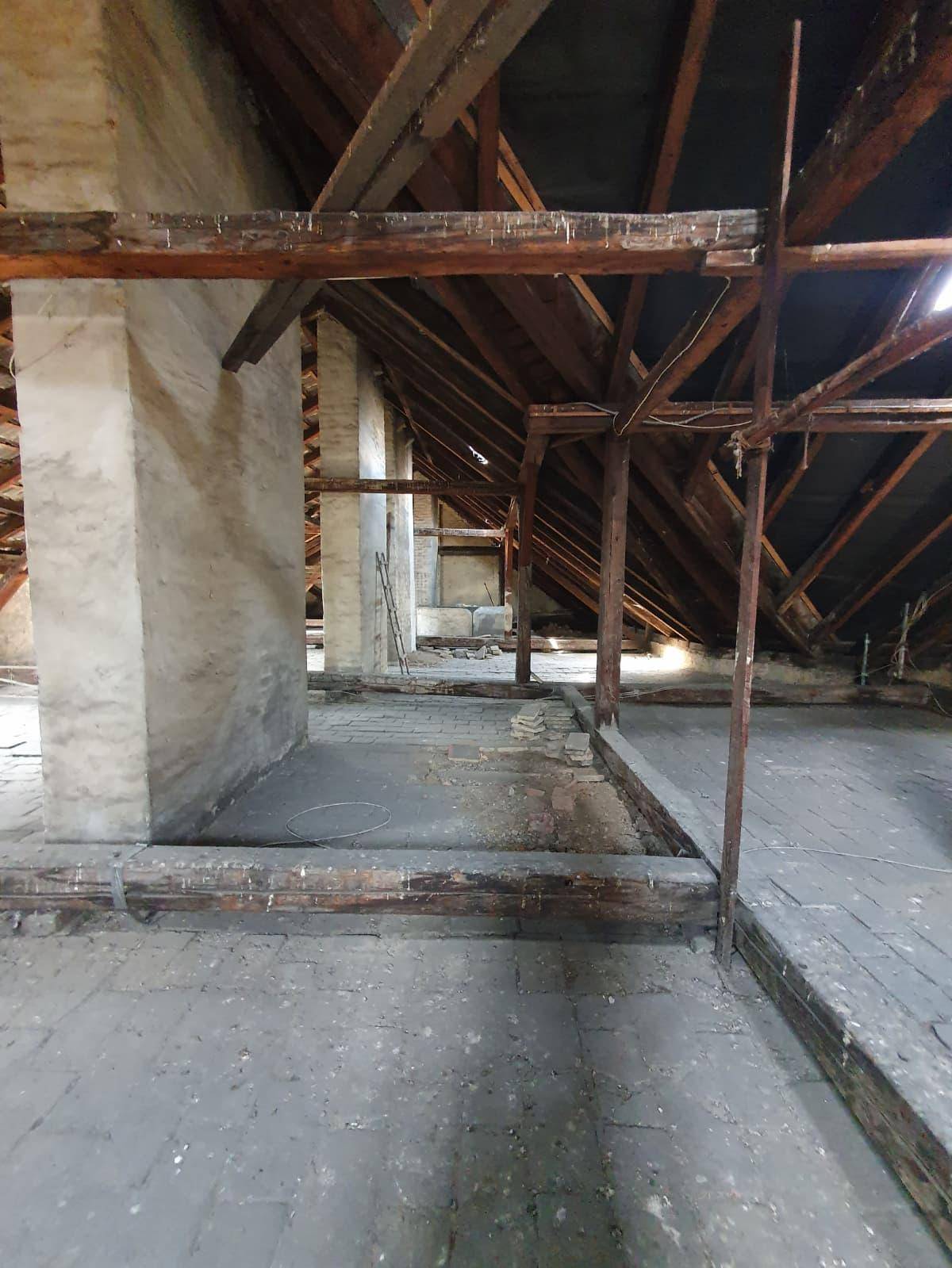 Großer Dachboden mit sichtbaren Holzbalken, Ziegelboden und einer massiven Säule, ideal für Umbau.